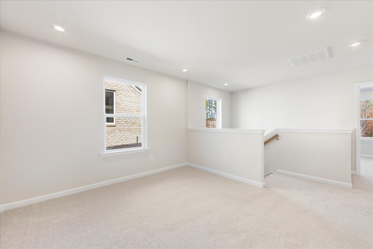 A bright, spacious room with white walls, recessed lighting, and a window providing natural light. The room appears to be a bedroom or living space with a clean, minimalist aesthetic.