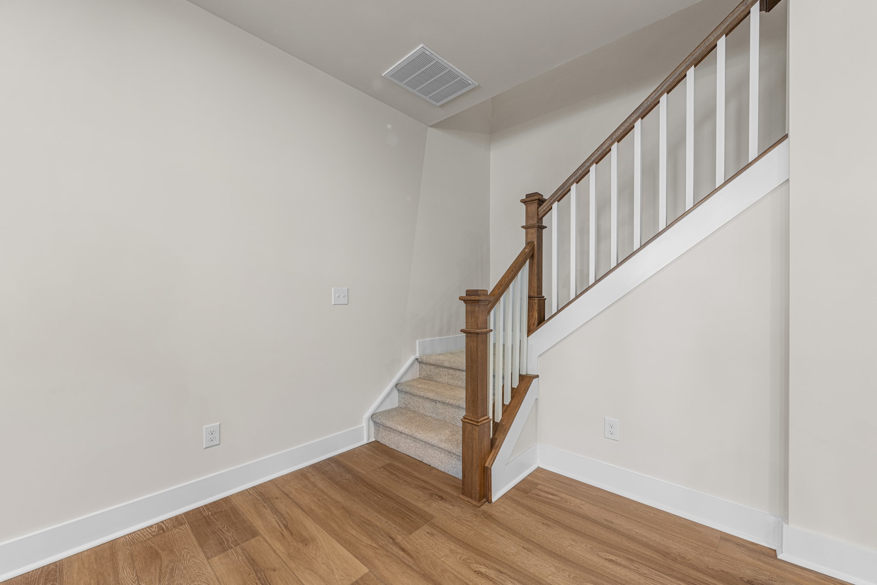 A staircase with wooden railings and steps leading up to a landing, set against a plain white wall in the background.