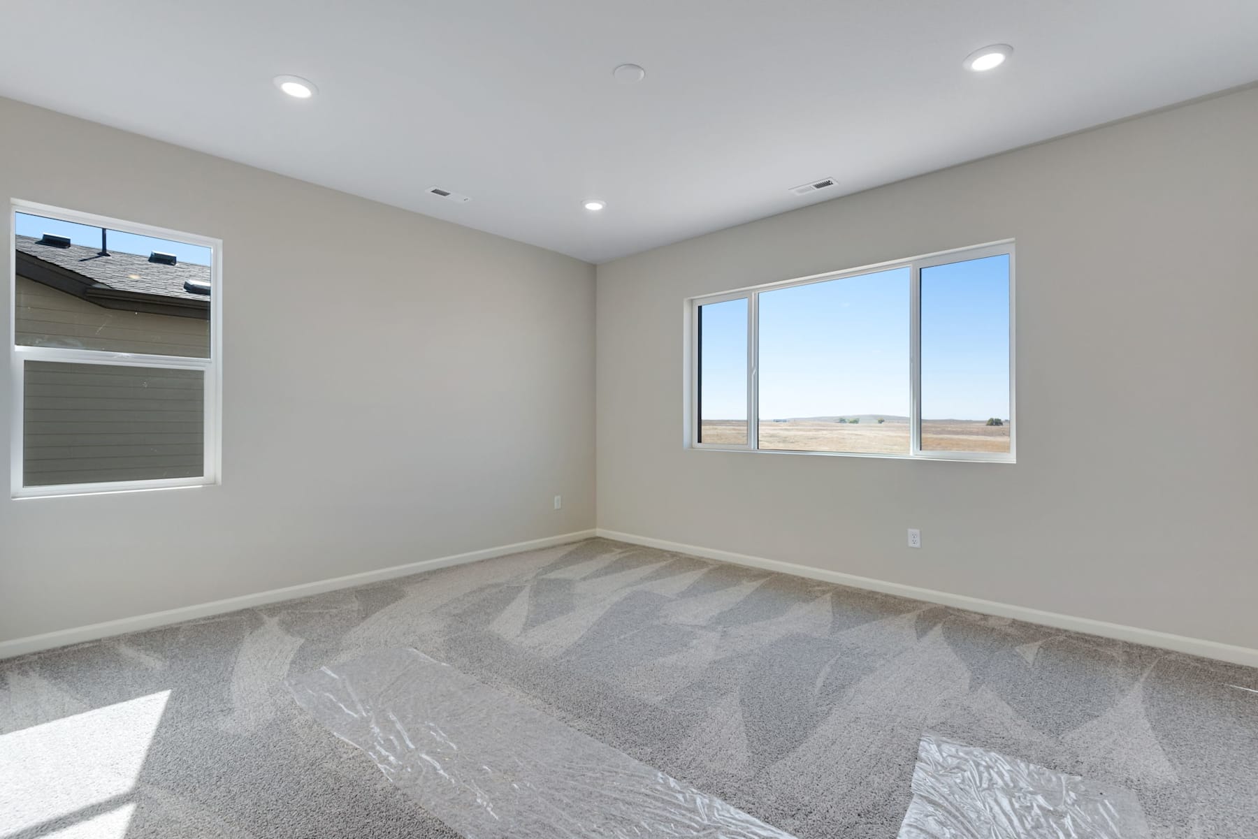 A spacious, well-lit room with a large window overlooking a scenic landscape, featuring a patterned tile floor and neutral-toned walls.