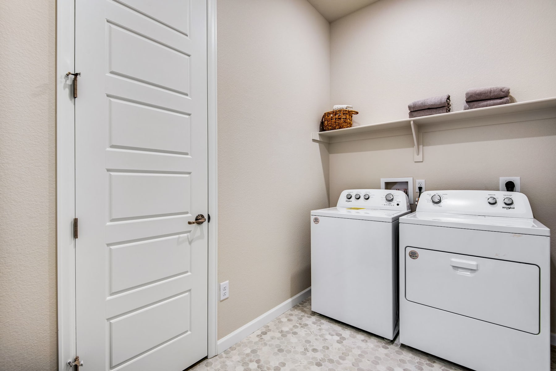 A small, well-organized laundry room with a white door, a washer and dryer, and shelves holding various items.