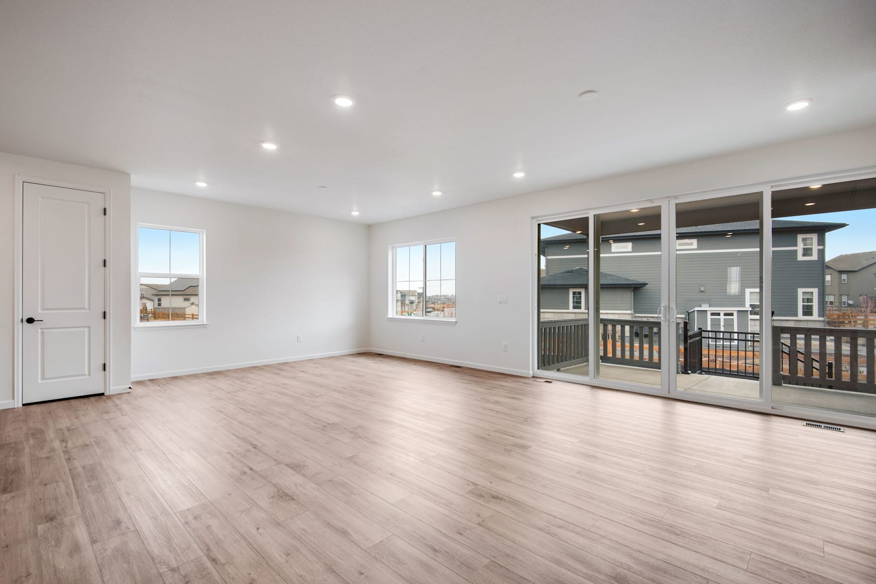 A spacious, well-lit room with hardwood floors, recessed lighting, and sliding glass doors leading to a balcony or deck.