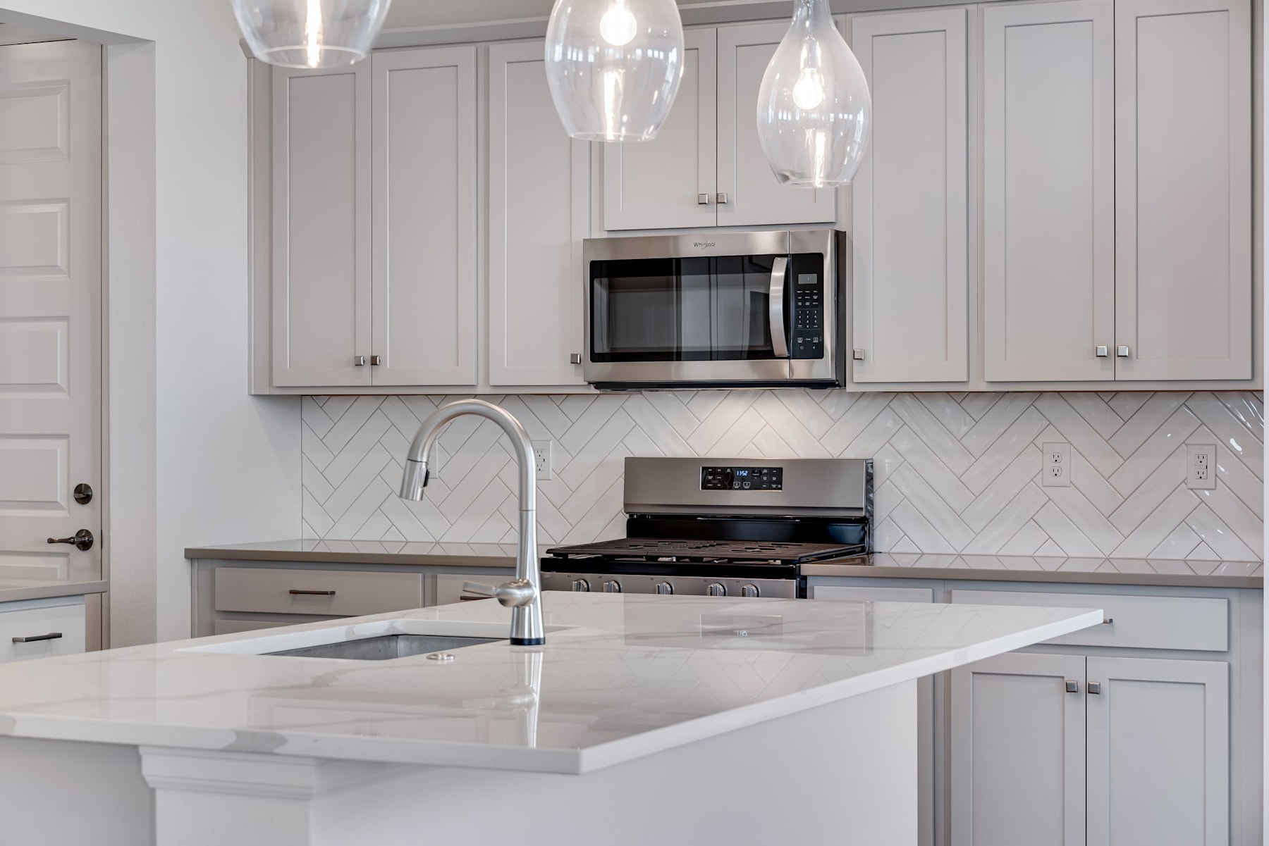 A modern, well-lit kitchen with gray cabinets, a white countertop, and pendant lights hanging above the island.