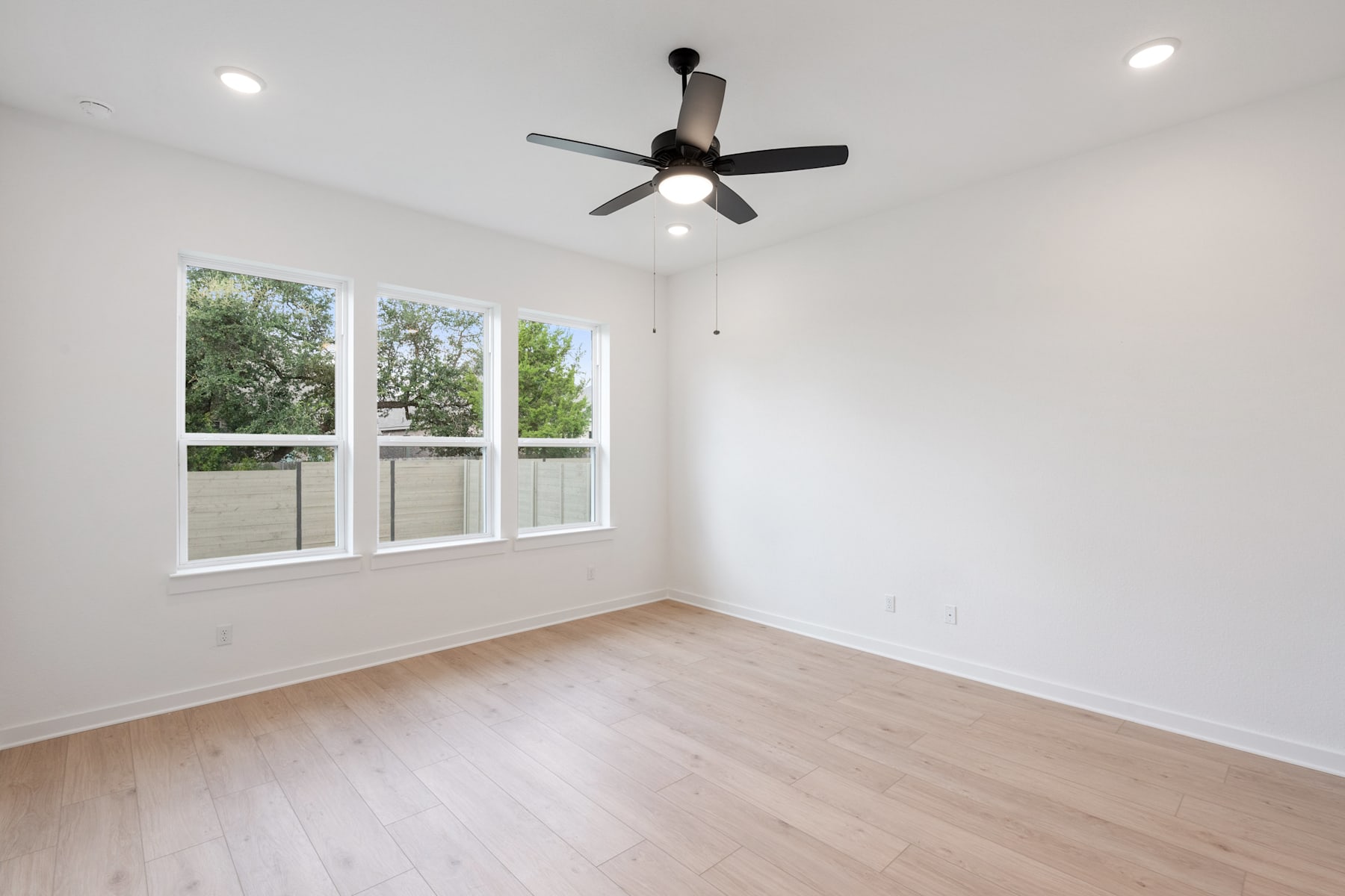 A bright, airy room with a ceiling fan and large windows overlooking a lush, green outdoor scene.