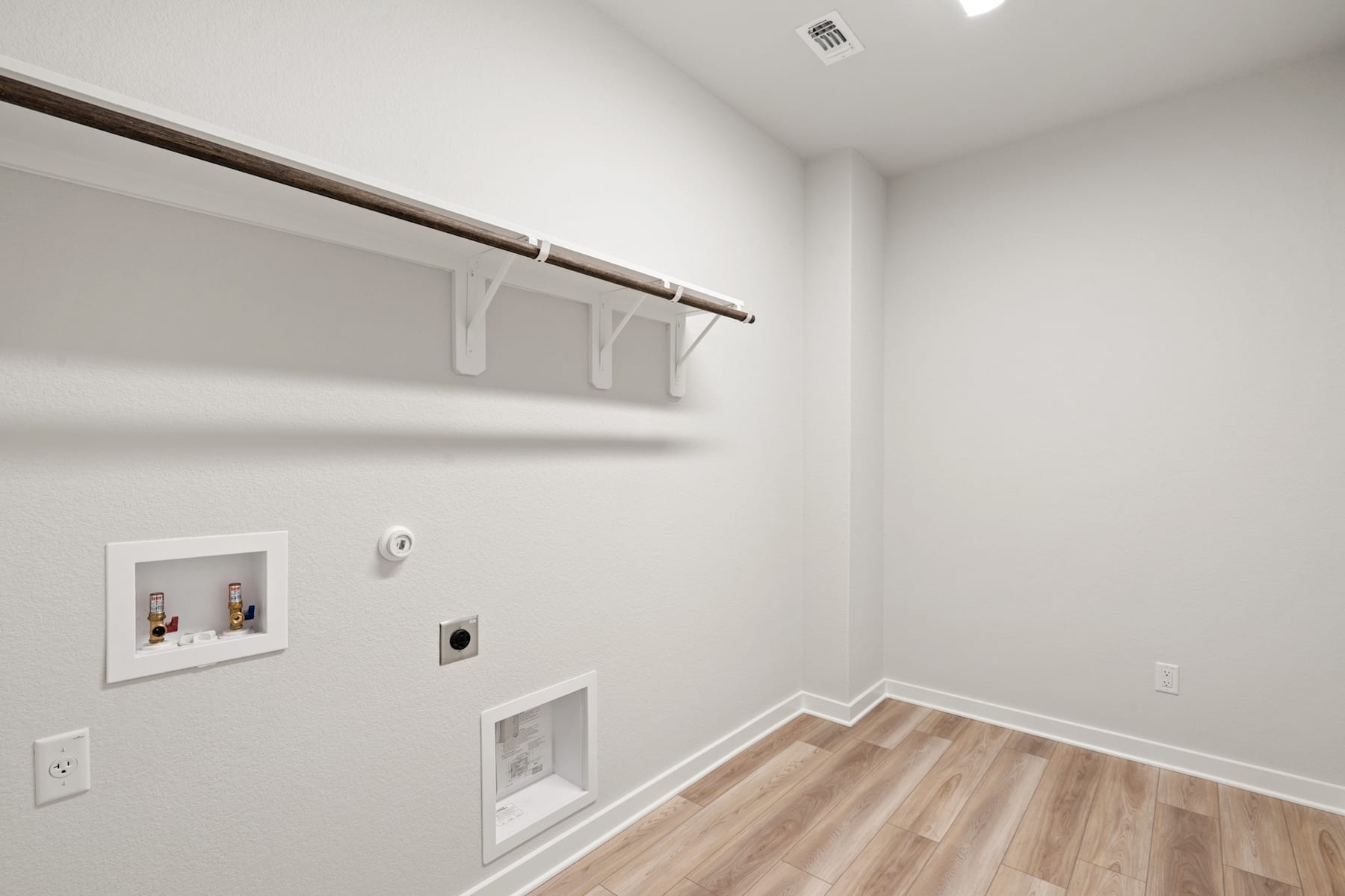 A minimalist, well-lit room with a wooden floor, white walls, and a hanging rod for storage or display.