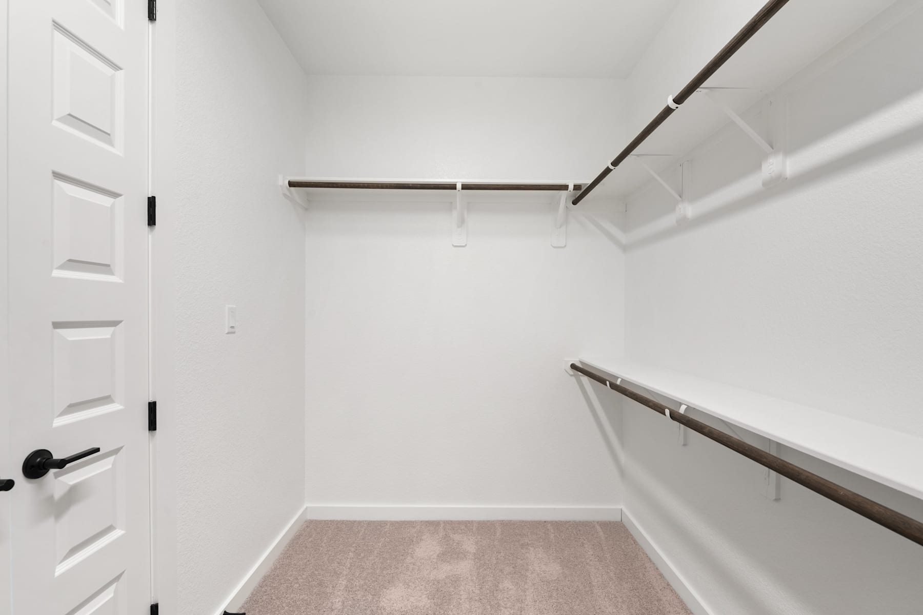 A white, minimalist closet space with a wooden clothing rod and shelves, featuring a closed door in the background.