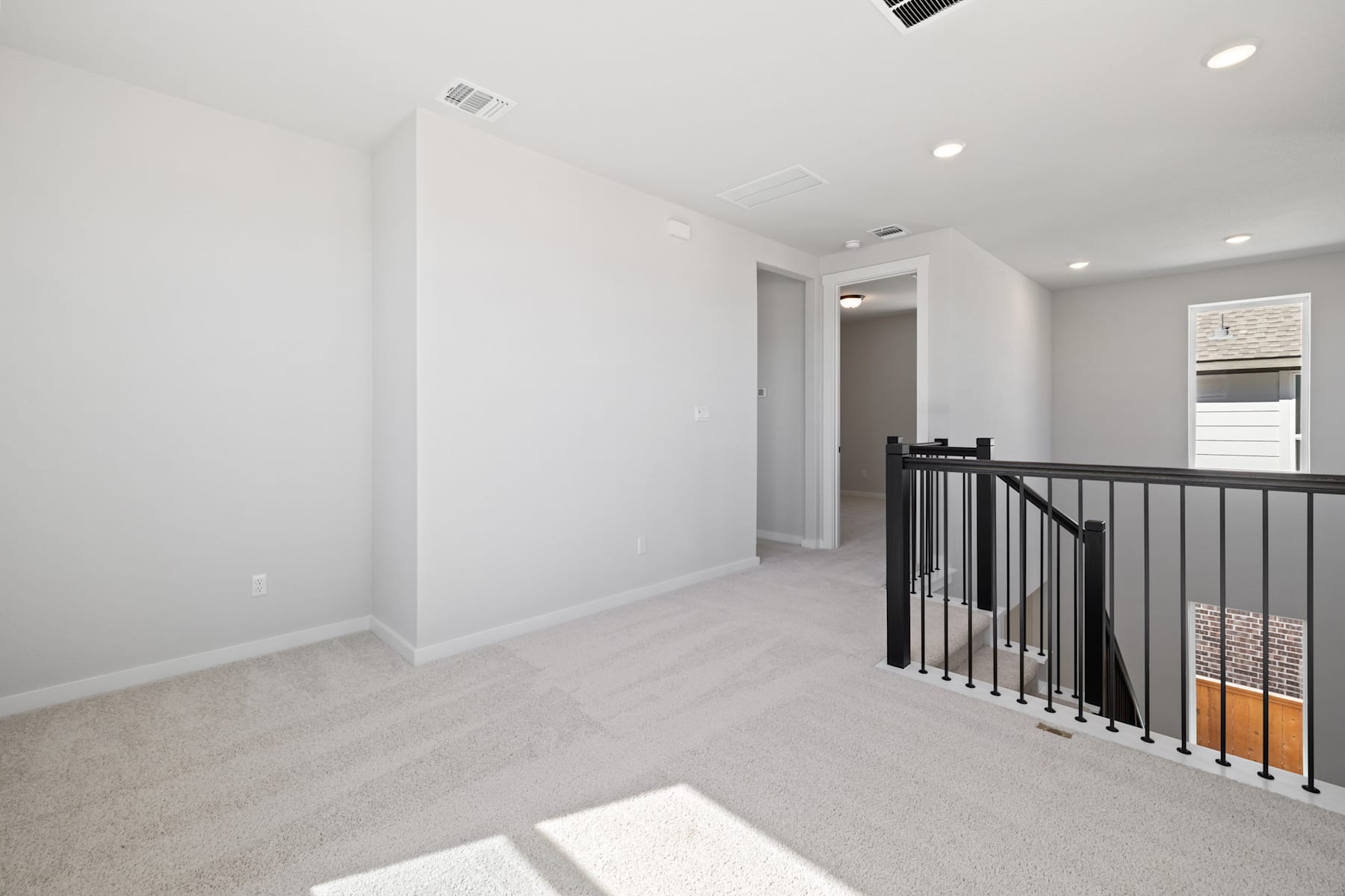 A bright, open hallway with a metal railing leading to a doorway, the walls painted in a neutral color and the floor covered in light-colored flooring.