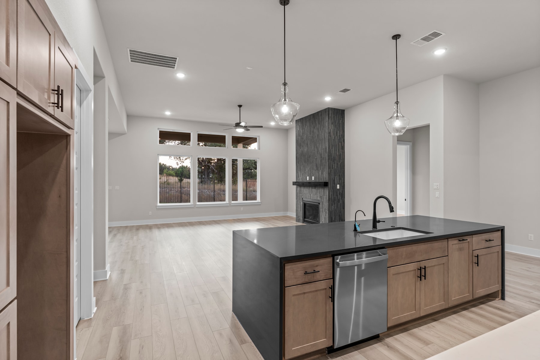 A modern, open-concept kitchen with a large island, stainless steel appliances, and pendant lighting, leading into a bright and airy living space with large windows.