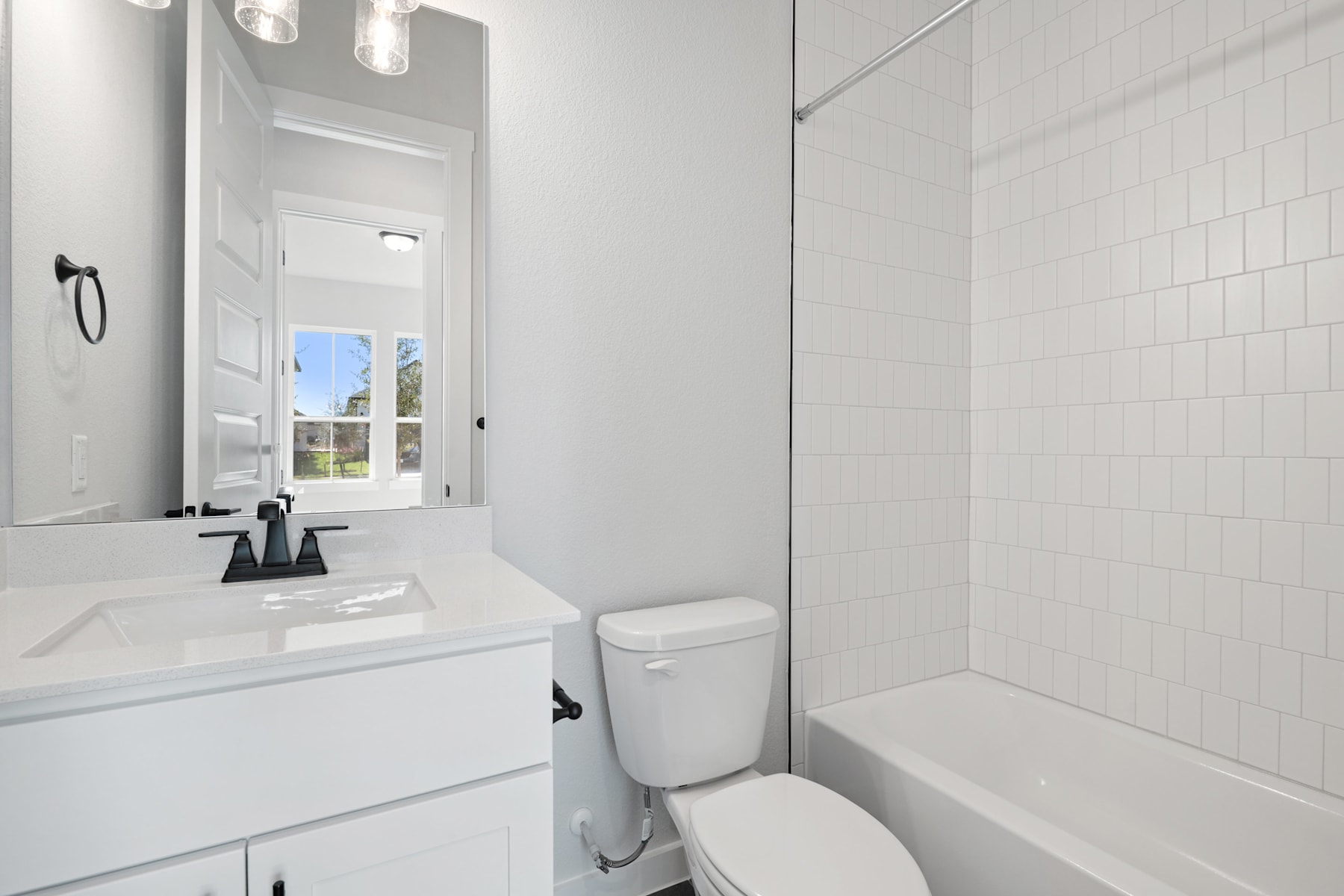 A modern, minimalist bathroom with a white vanity, toilet, and tiled walls, with a window providing natural light.