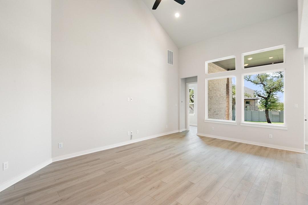 A bright and spacious room with hardwood floors, a large window overlooking a tree, and a minimalist design aesthetic.