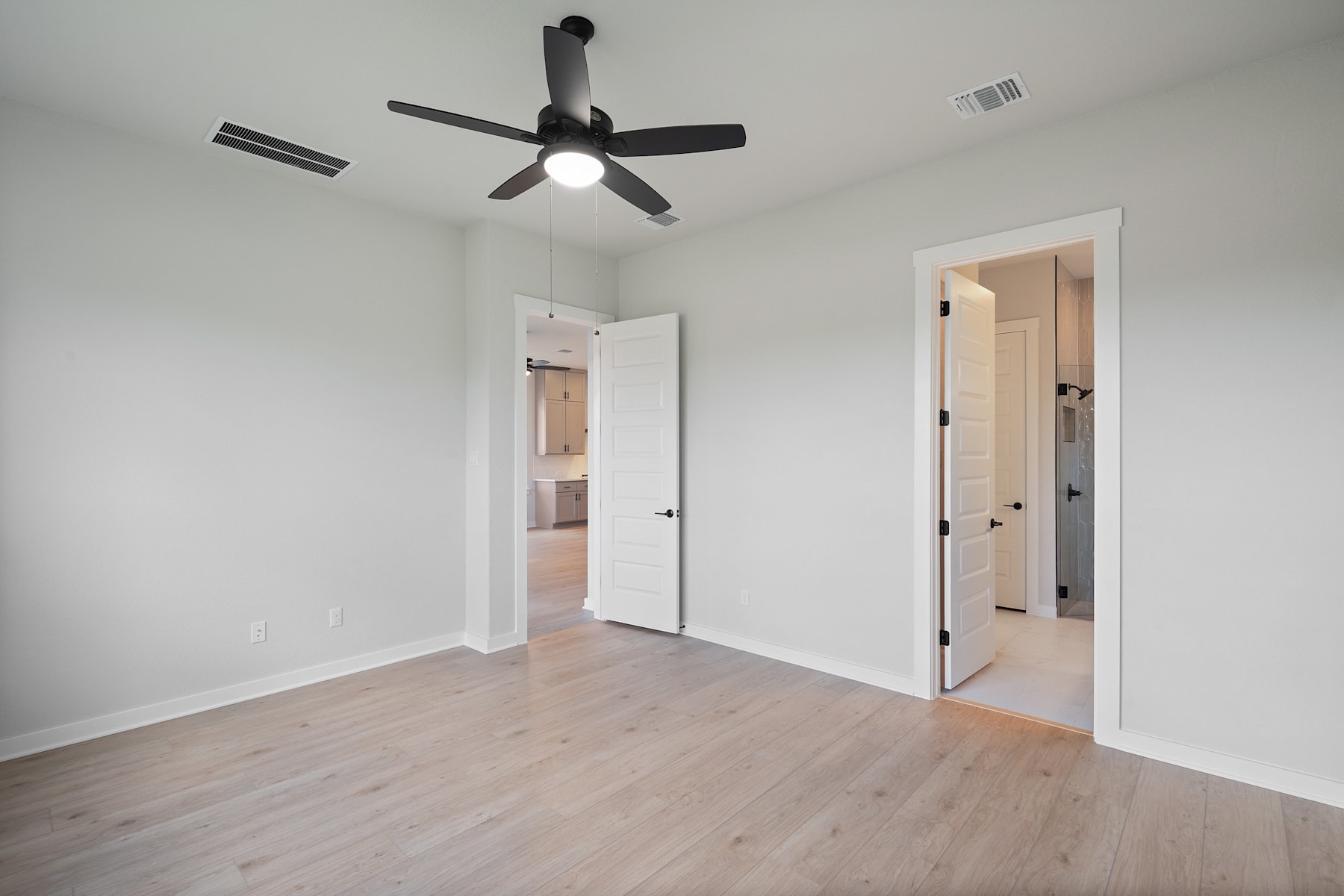 A simple, minimalist bedroom with a ceiling fan, white walls, and hardwood flooring.
