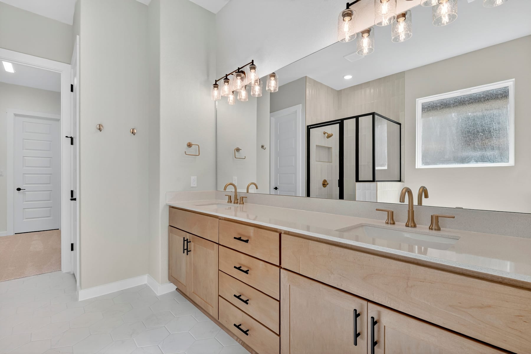 A modern and spacious bathroom with a double vanity, wooden cabinets, and a sleek, minimalist design featuring a chandelier and recessed lighting.