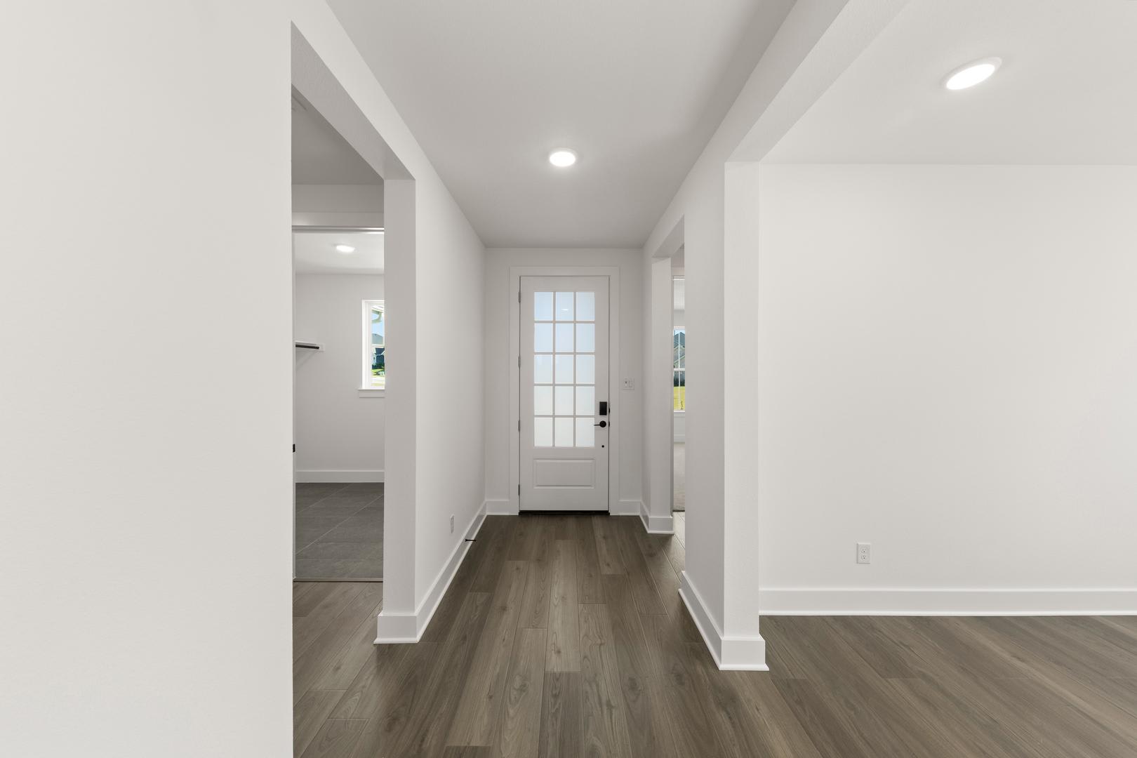 A bright, spacious hallway with a wooden floor and a glass-paneled door leading to another room.