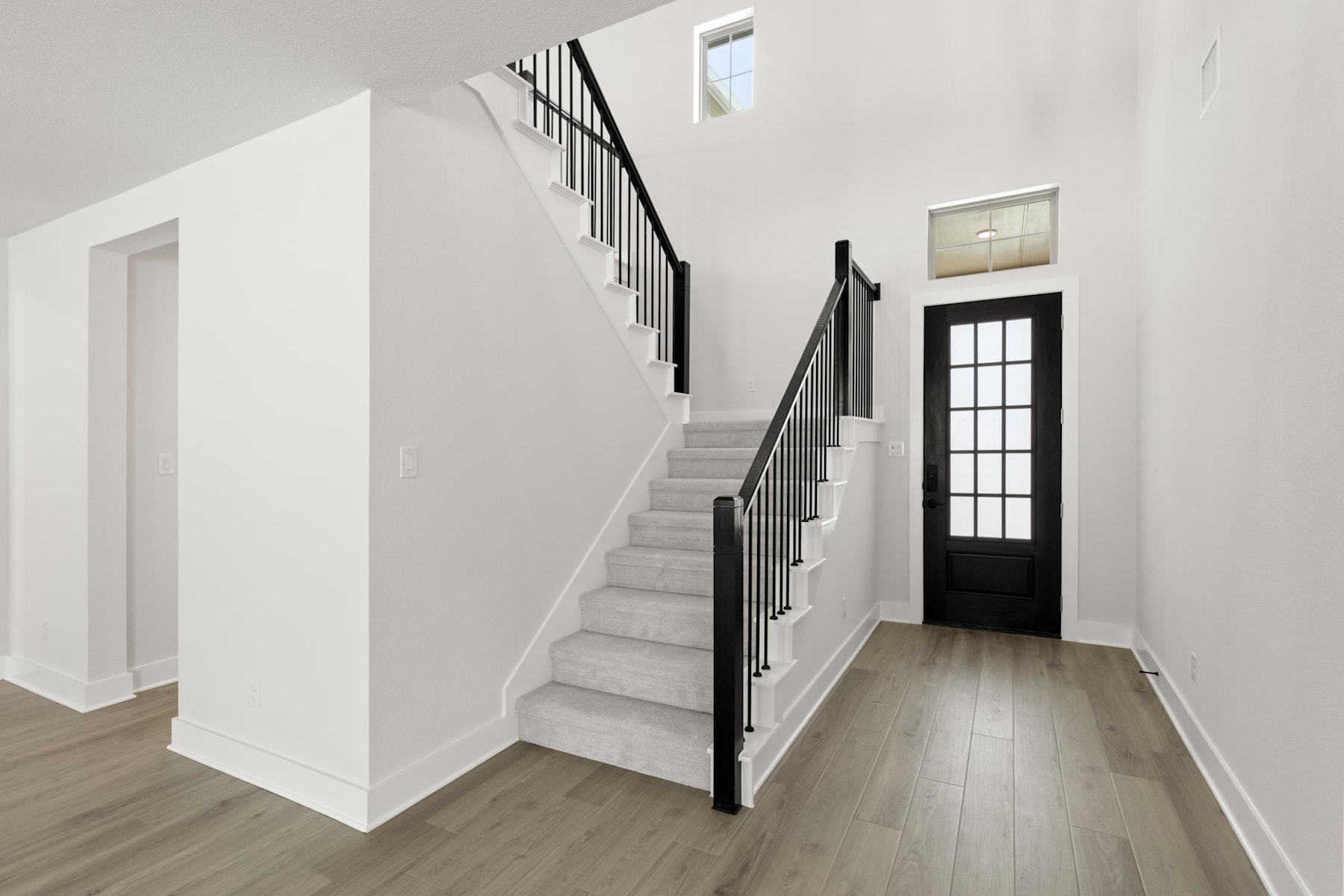 A modern, minimalist staircase with black metal railings leads up to a second floor, with a wooden floor and a glass-paneled door visible in the background.