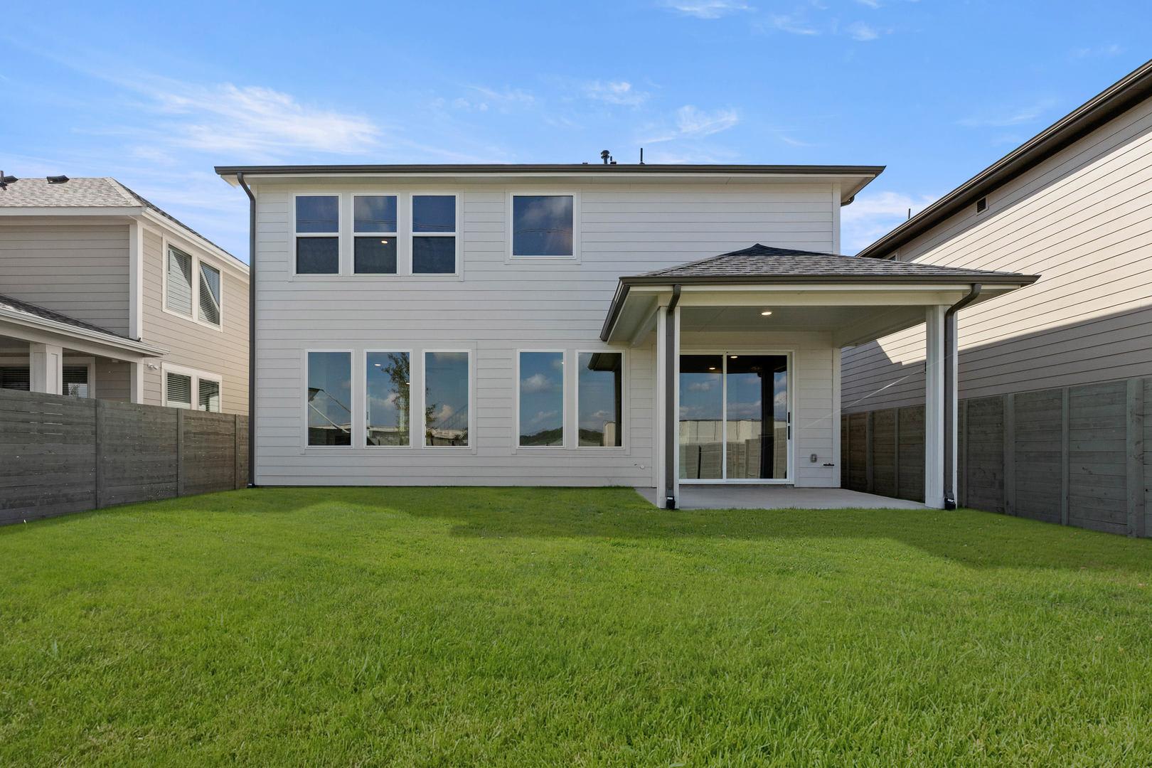 A modern two-story house with a large grassy yard in the foreground, surrounded by other residential buildings in the background.