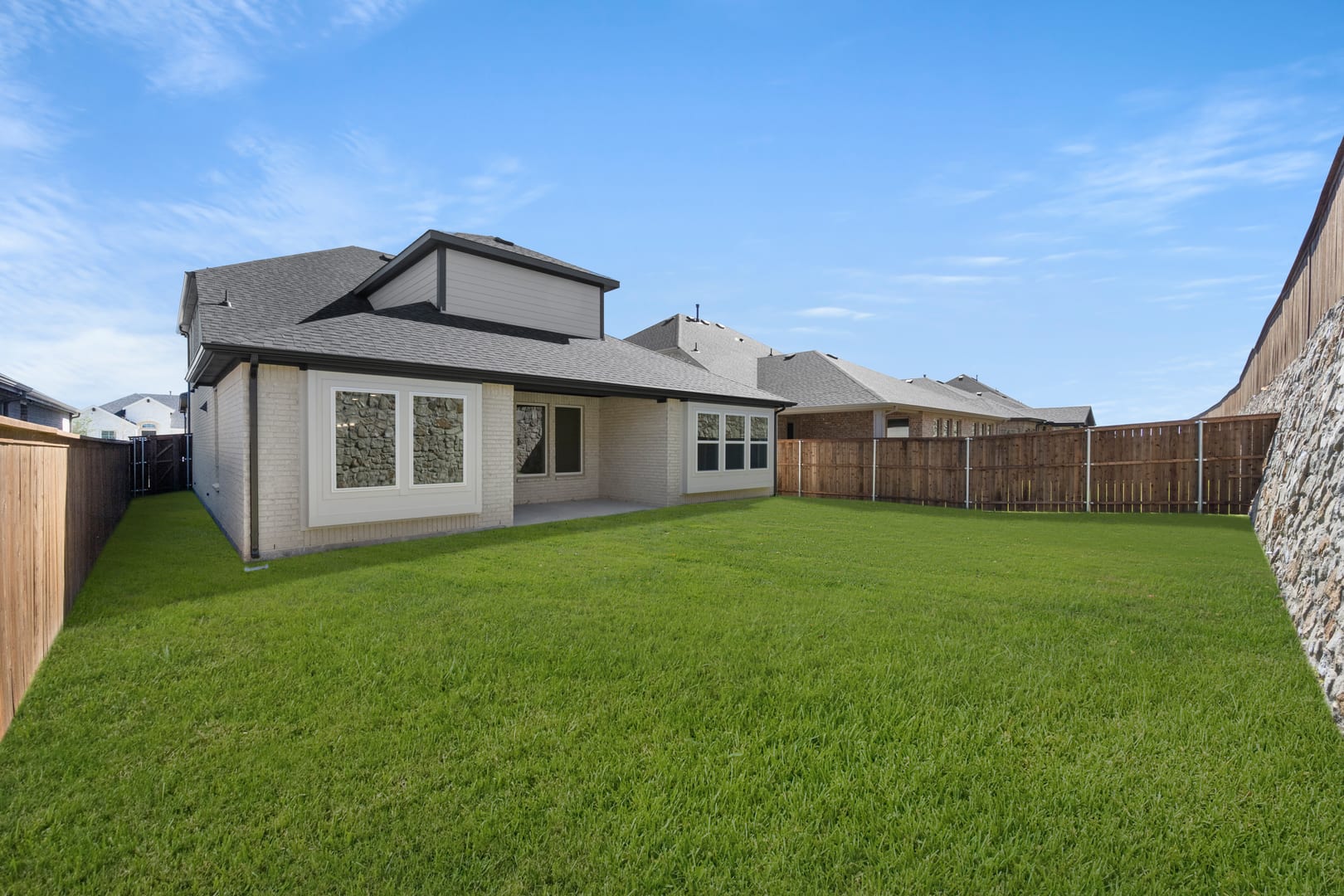 A well-manicured lawn stretches out in the foreground, surrounded by a wooden fence, leading to a modern, two-story house with a gabled roof and large windows in the background.