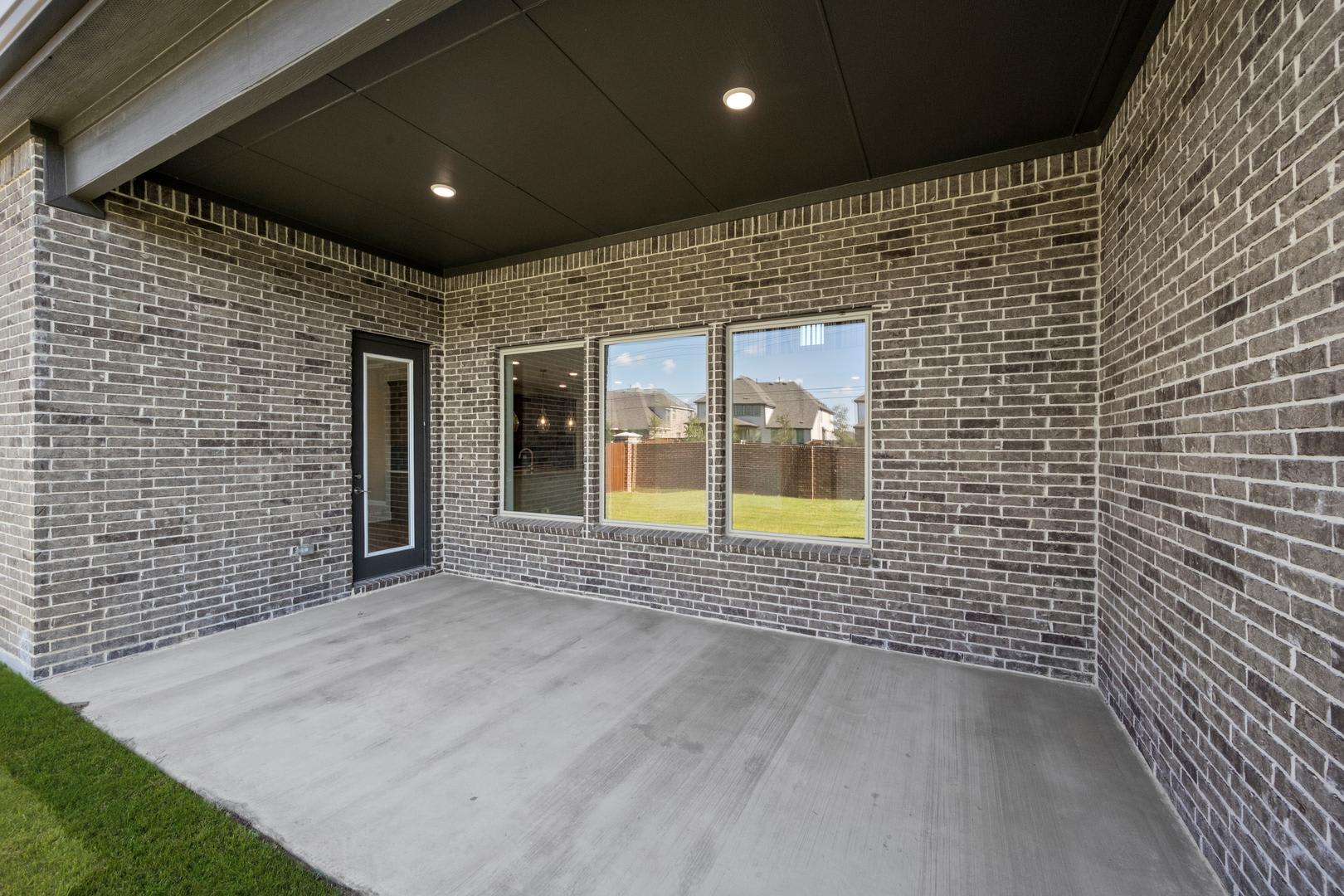 A covered patio with a brick exterior, featuring large windows that provide a view of the surrounding landscape.