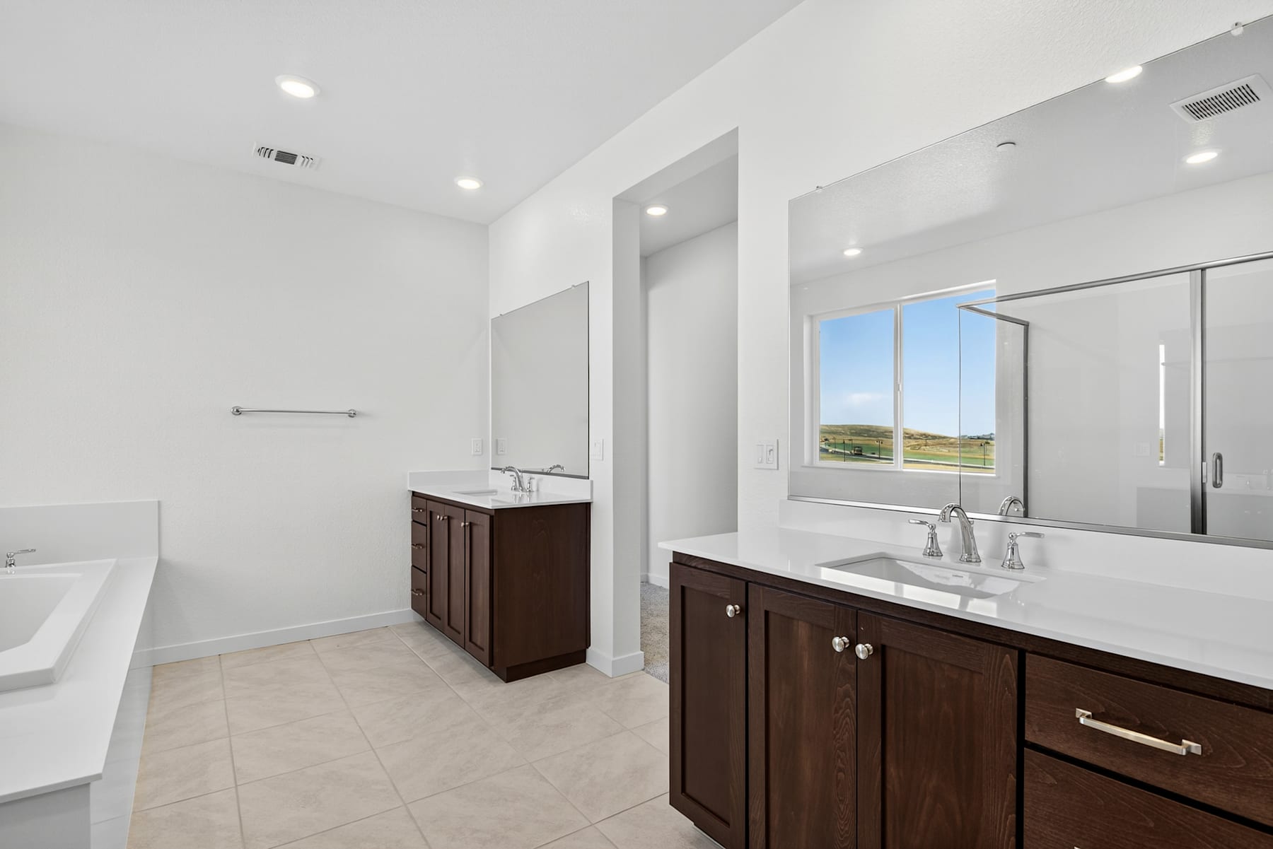 A modern and spacious bathroom with dark wood cabinets, a large mirror, and a window overlooking a scenic outdoor landscape.