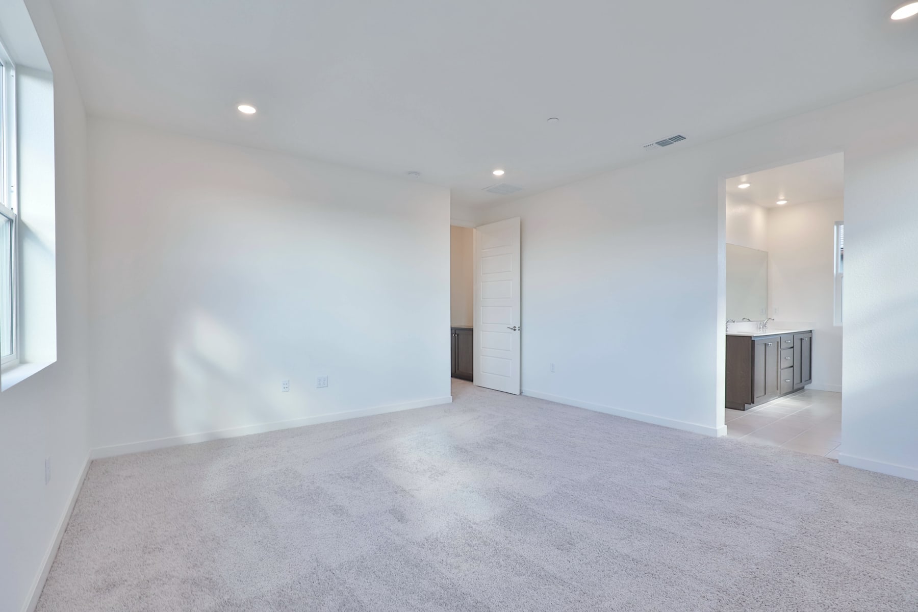A spacious, minimalist room with white walls, a hardwood floor, and a doorway leading to another room.