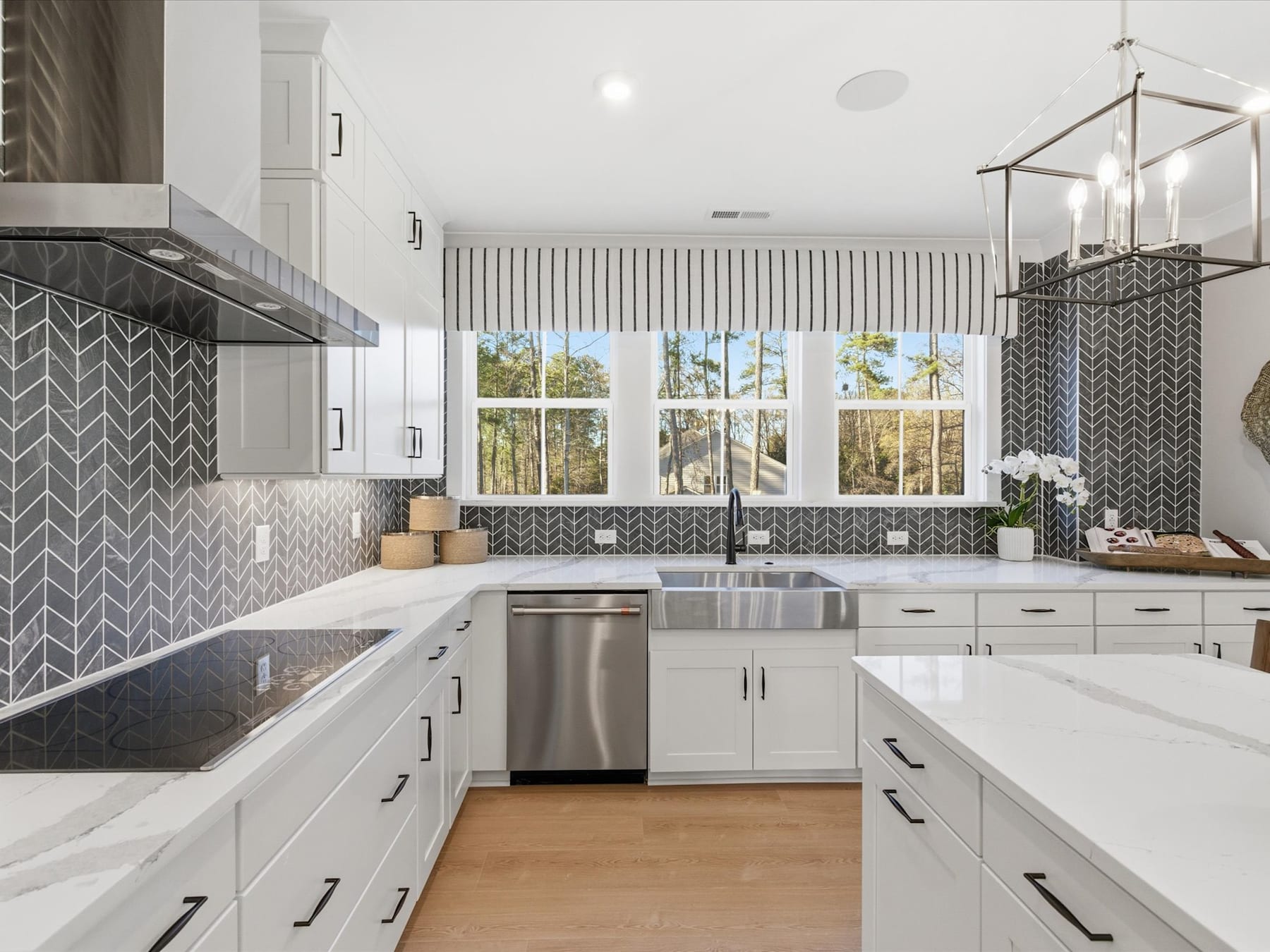 A modern, well-lit kitchen with white cabinets, stainless steel appliances, and a patterned backsplash, overlooking a scenic outdoor view through large windows.