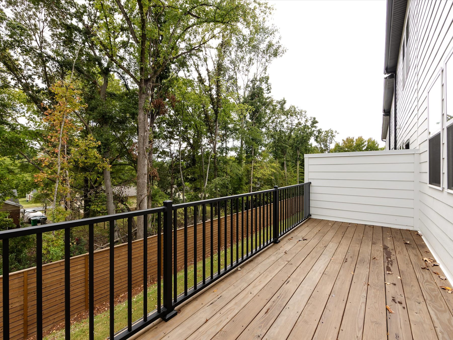 A wooden deck with a metal railing overlooks a lush, forested area with tall trees and greenery in the background.