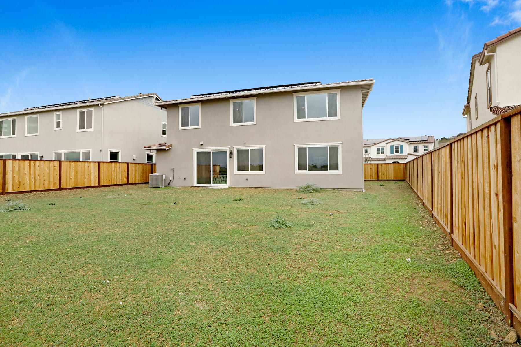 A two-story residential building with a fenced backyard and a well-maintained lawn in the foreground, set against a clear blue sky.
