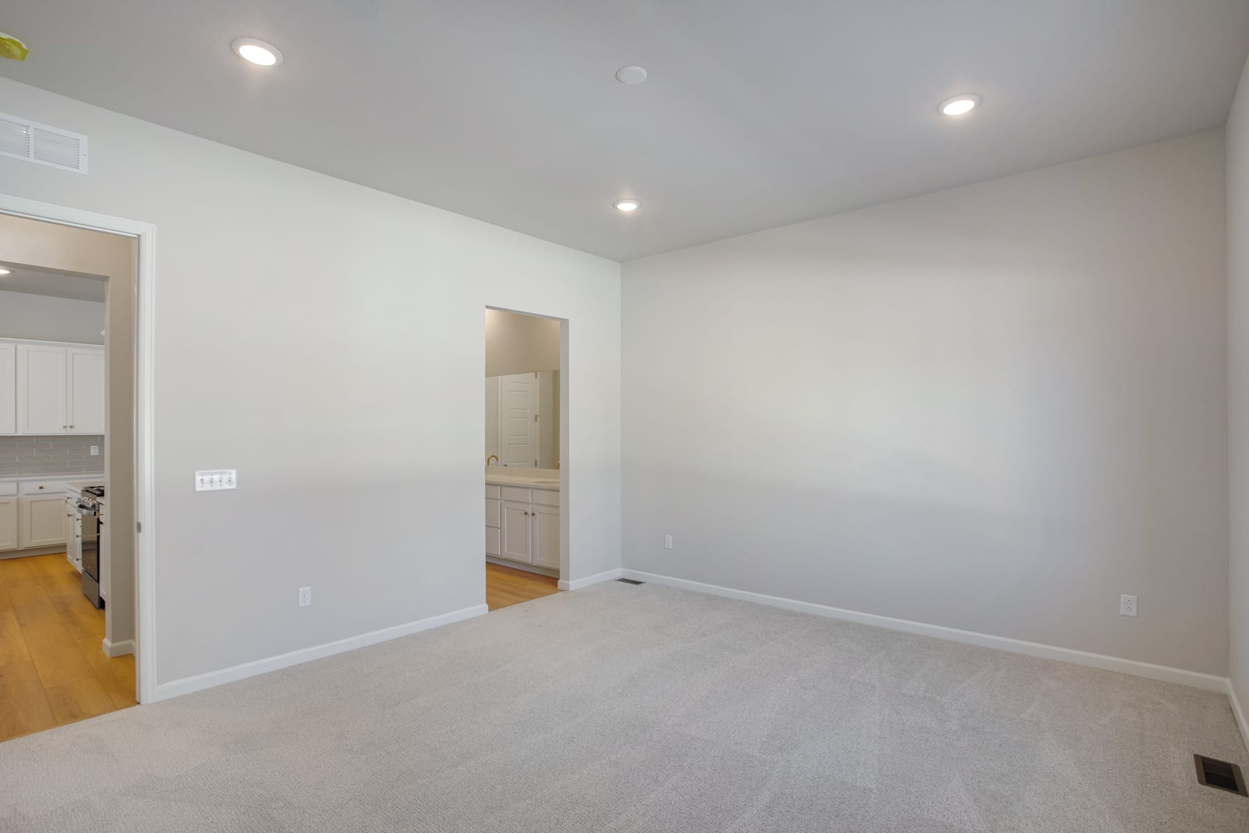 A spacious, well-lit room with white walls, a carpeted floor, and recessed lighting fixtures in the ceiling.