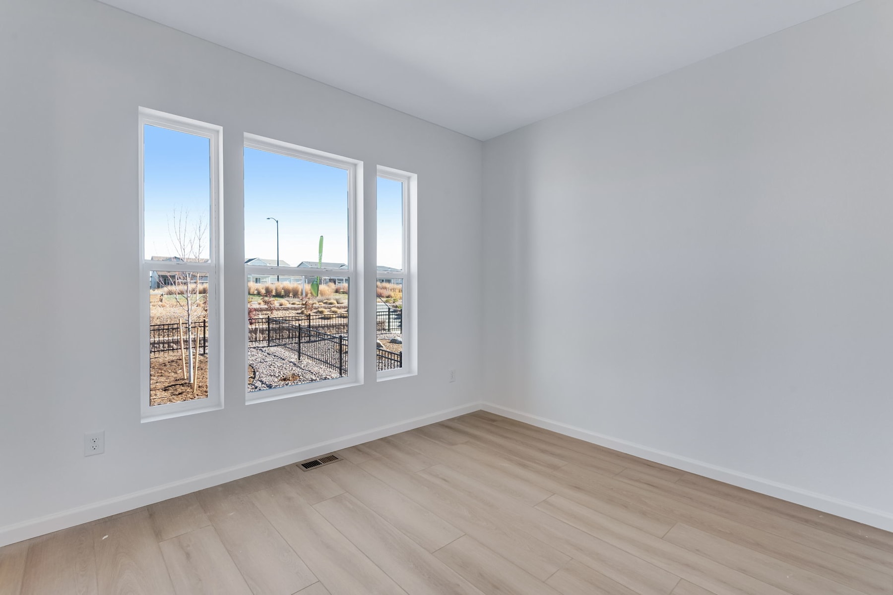 A bright and spacious room with large windows overlooking a construction site in the background, featuring a hardwood floor and plain white walls.