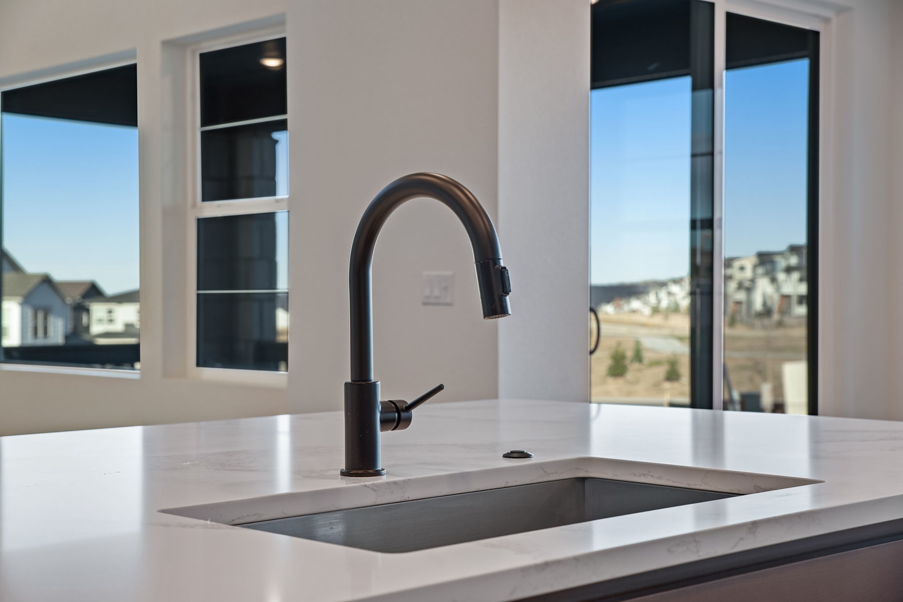 A modern kitchen sink with a black faucet and a large window overlooking a cityscape in the background.