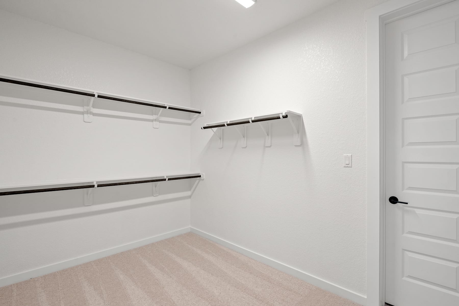 A simple, minimalist closet space with white walls, wooden flooring, and a clothing rod with hangers.