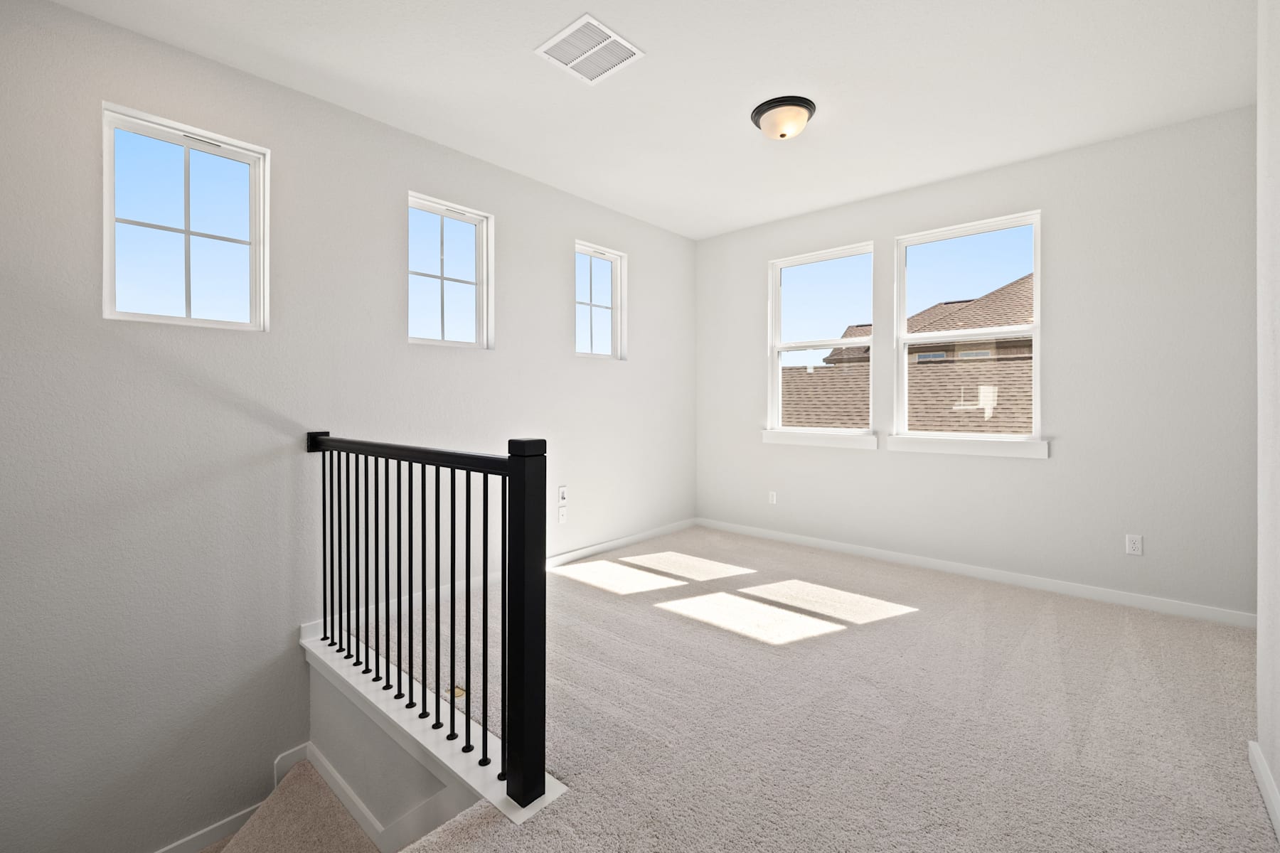 A bright and airy room with a staircase railing in the foreground and large windows allowing natural light to flood the space.