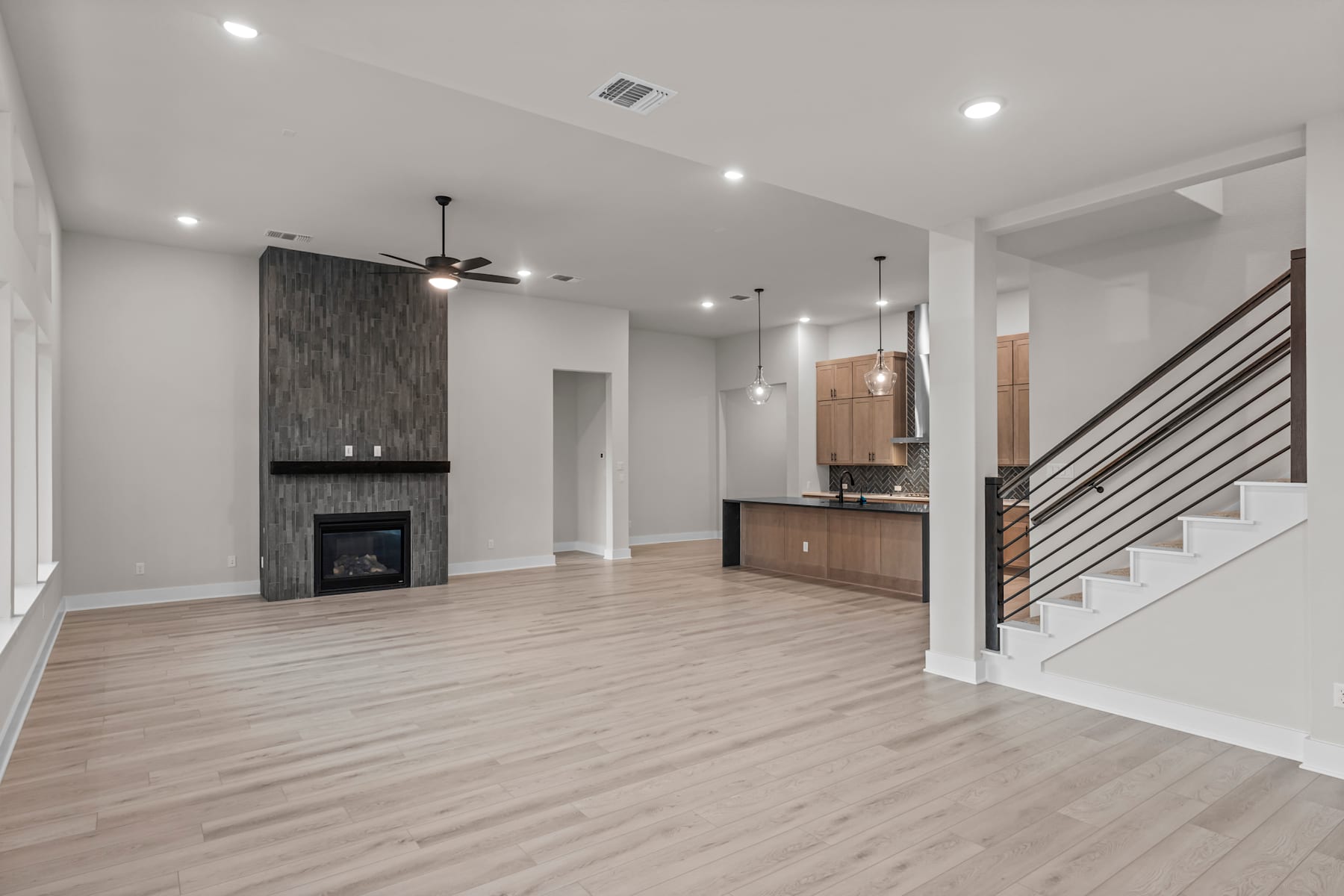 A modern, open-concept living space with a fireplace, wooden floors, and a staircase leading to an upper level.