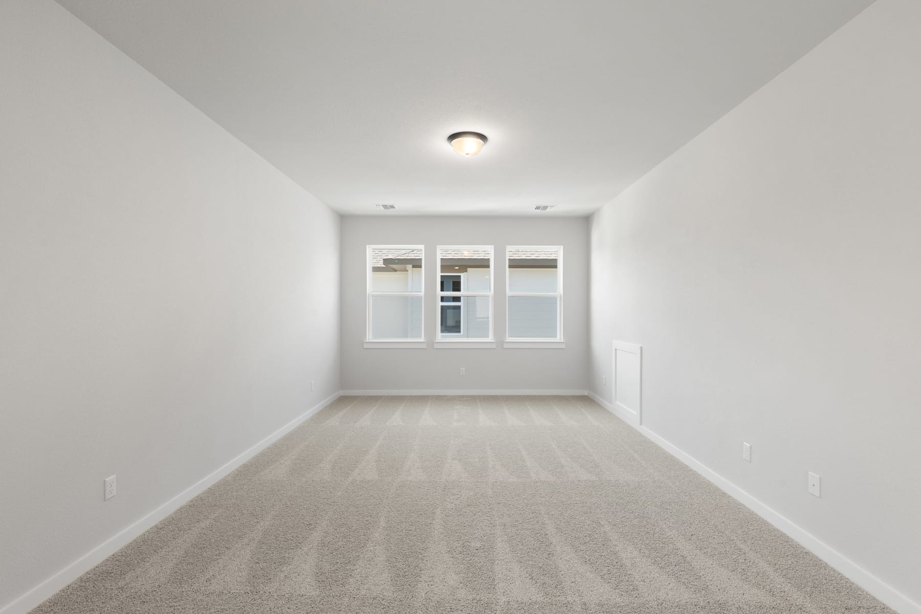 A bright, minimalist room with a plain white wall, a light fixture, and a hardwood floor.