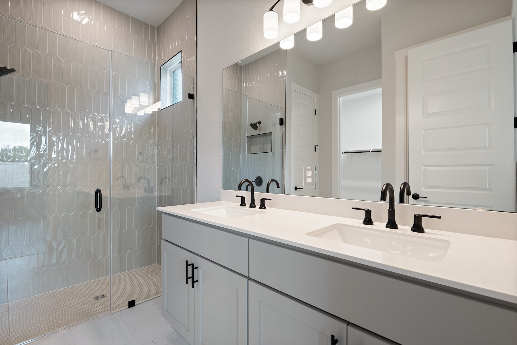 A modern and sleek bathroom with a double vanity, white countertop, and black fixtures, set against a backdrop of white subway tiles and recessed lighting.