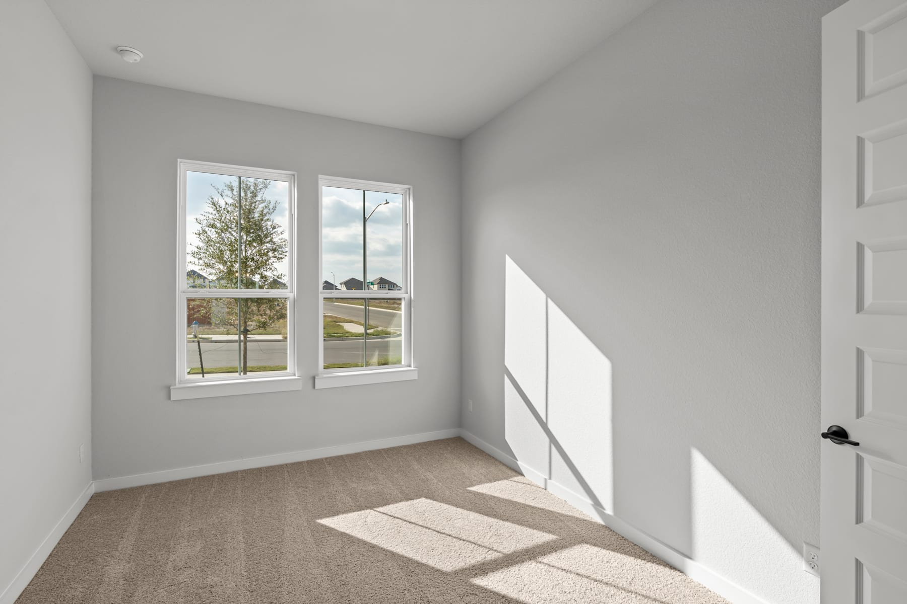 A bright and airy room with large windows overlooking a snowy outdoor scene, featuring a bare hardwood floor and a white wall with a door.