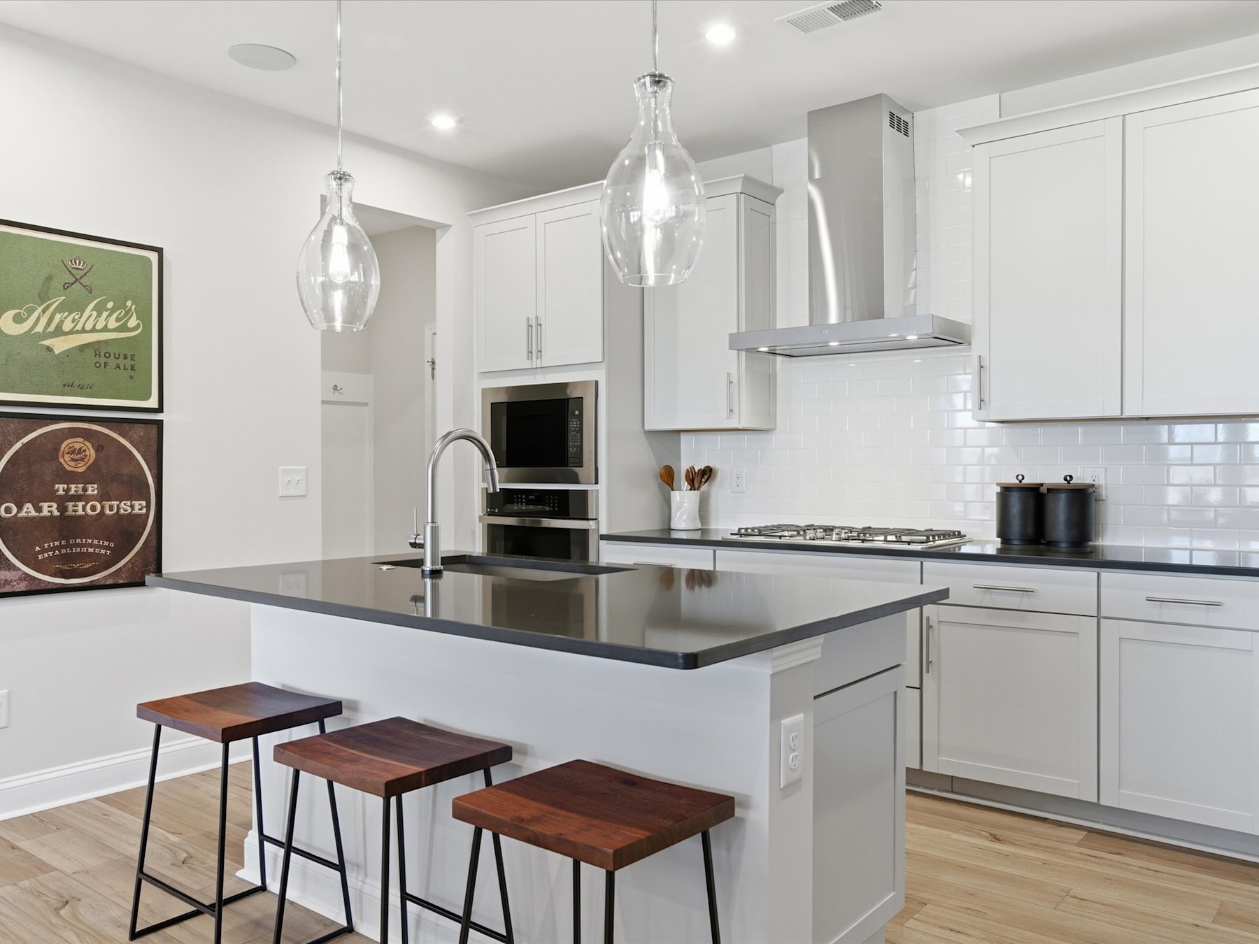 A modern, well-lit kitchen with white cabinets, a central island with stools, and pendant lights hanging above, creating a sleek and stylish atmosphere.