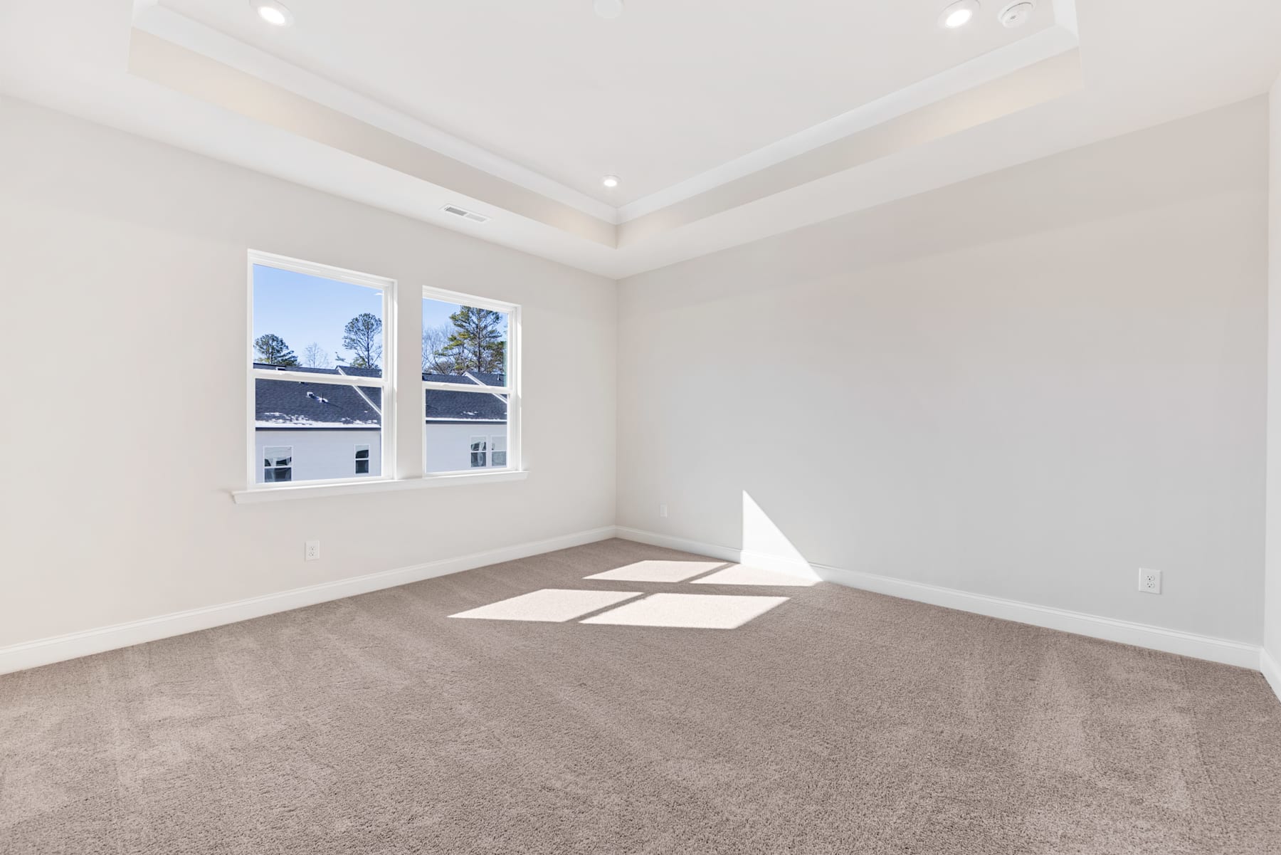 A bright and spacious room with large windows, a vaulted ceiling, and a neutral-toned carpet covering the floor.