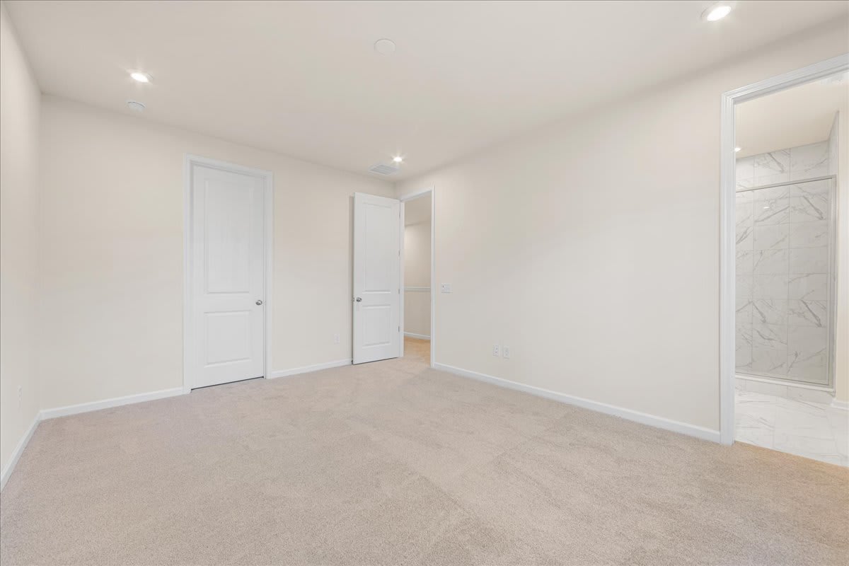 A spacious, minimalist room with white walls, a light-colored hardwood floor, and two closed doors leading to other areas.