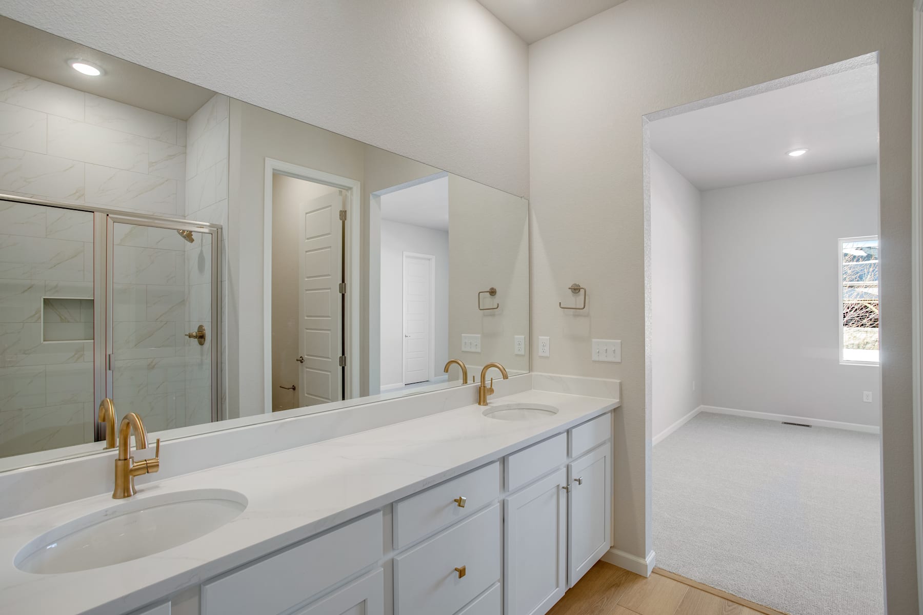 A modern, well-lit bathroom with a large vanity, double sinks, and a glass-enclosed shower area. The room features neutral-toned walls and floors, creating a clean and minimalist aesthetic.
