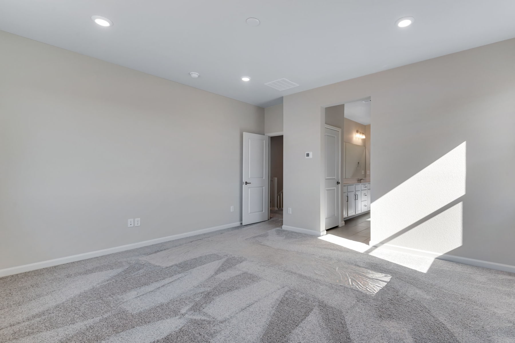 A spacious, minimalist room with gray walls, a white door, and a patterned gray carpet covering the floor.