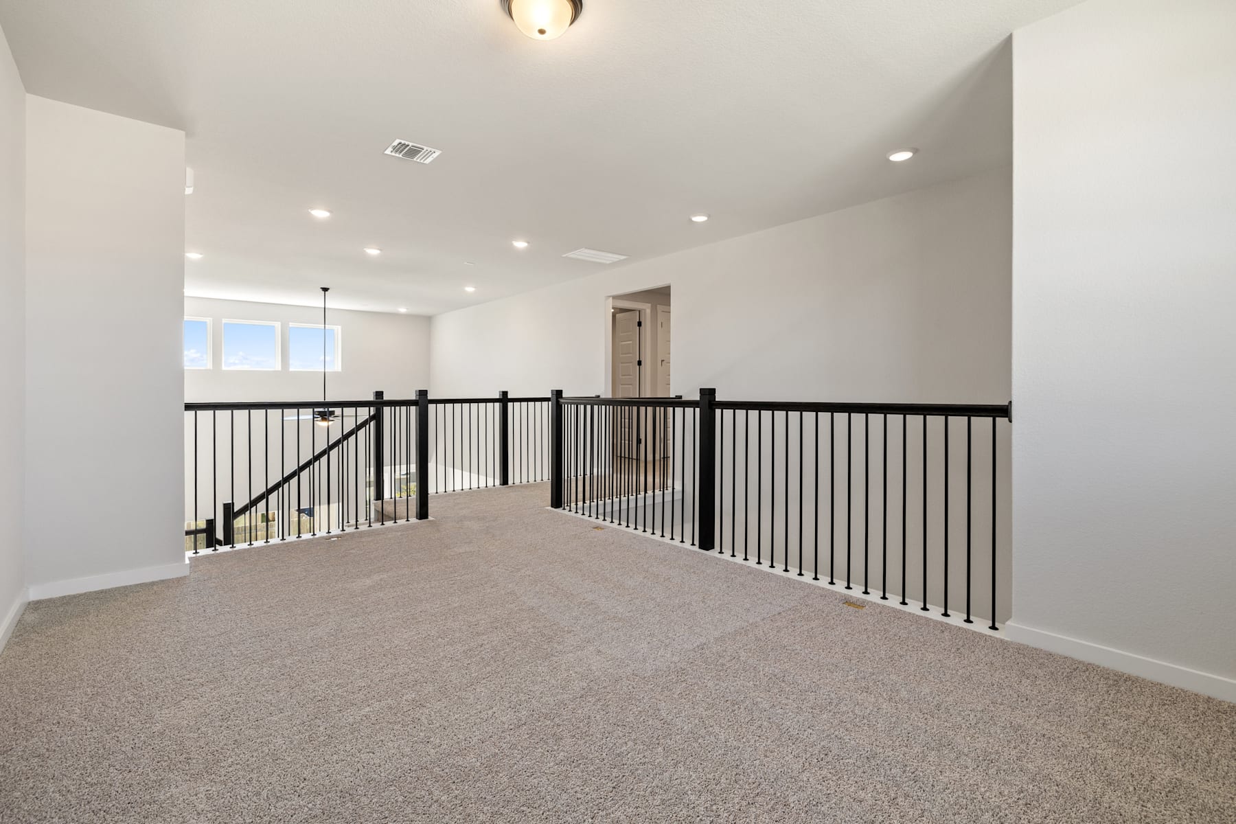 A spacious, well-lit room with a carpeted floor and a metal railing running along the upper level, leading to a doorway in the background.