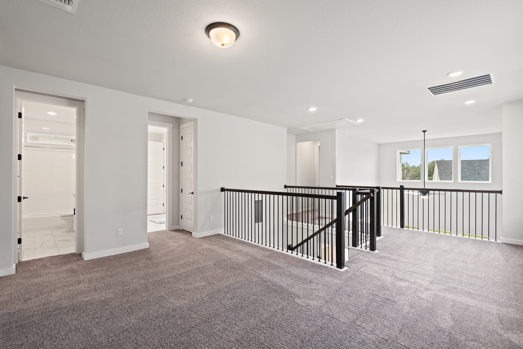 A spacious, well-lit room with a carpeted floor, a railing, and several doors leading to other areas of the home.