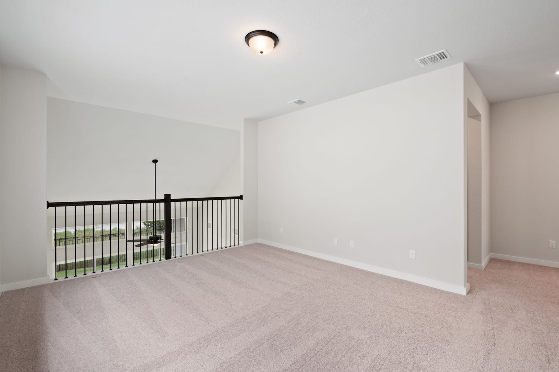 A spacious, well-lit room with a white wall, a ceiling light fixture, and a metal railing leading to an unseen area.