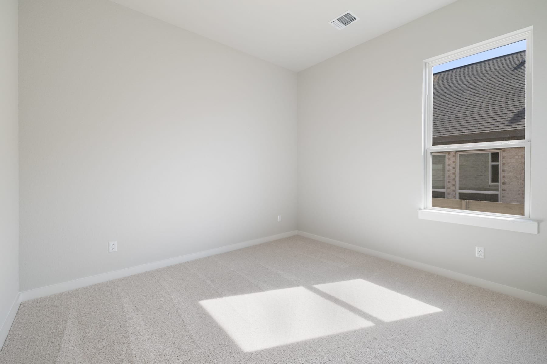 An empty, well-lit room with a window, featuring a plain white wall and a tiled floor.