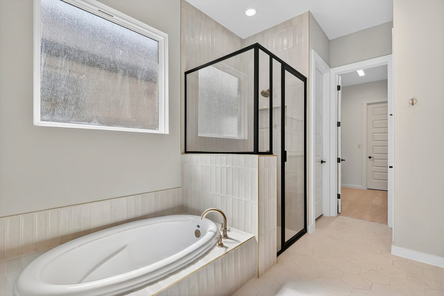 A modern bathroom with a large oval bathtub, a glass-enclosed shower, and a hallway leading to other rooms in the home.