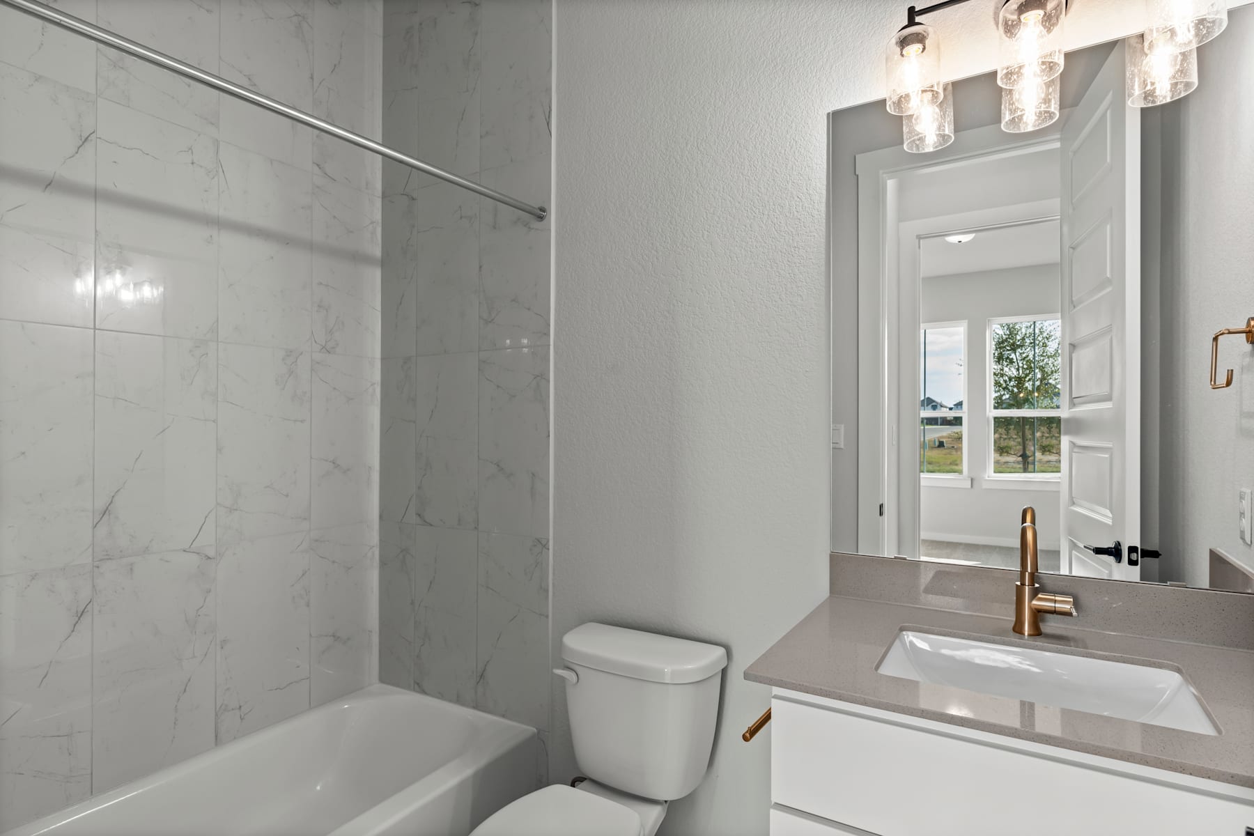 A modern, minimalist bathroom with a white vanity, a large mirror, and a glass shower enclosure, illuminated by a stylish chandelier.