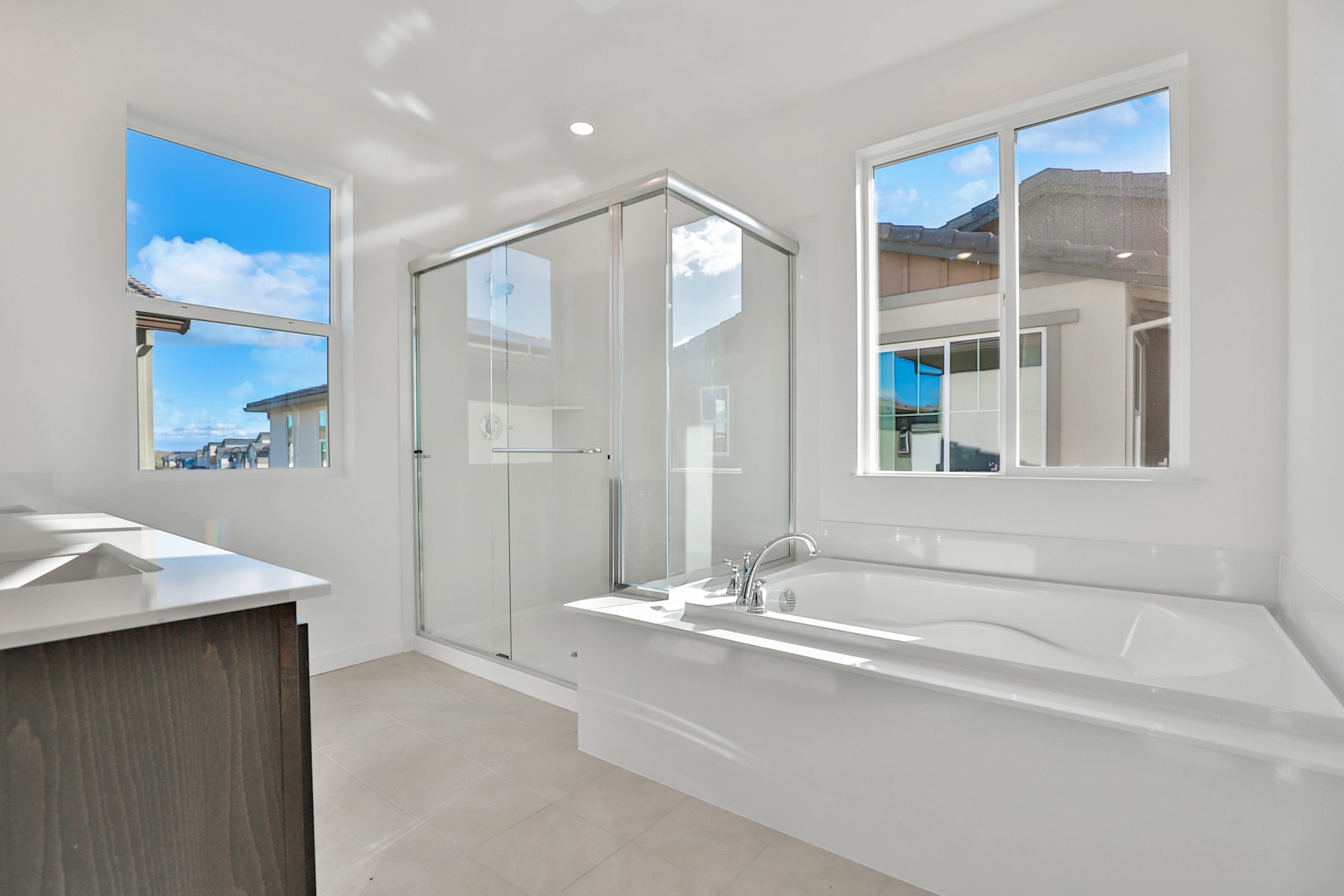 A modern, bright bathroom with a large bathtub, vanity, and windows providing a view of the sky and surrounding buildings.