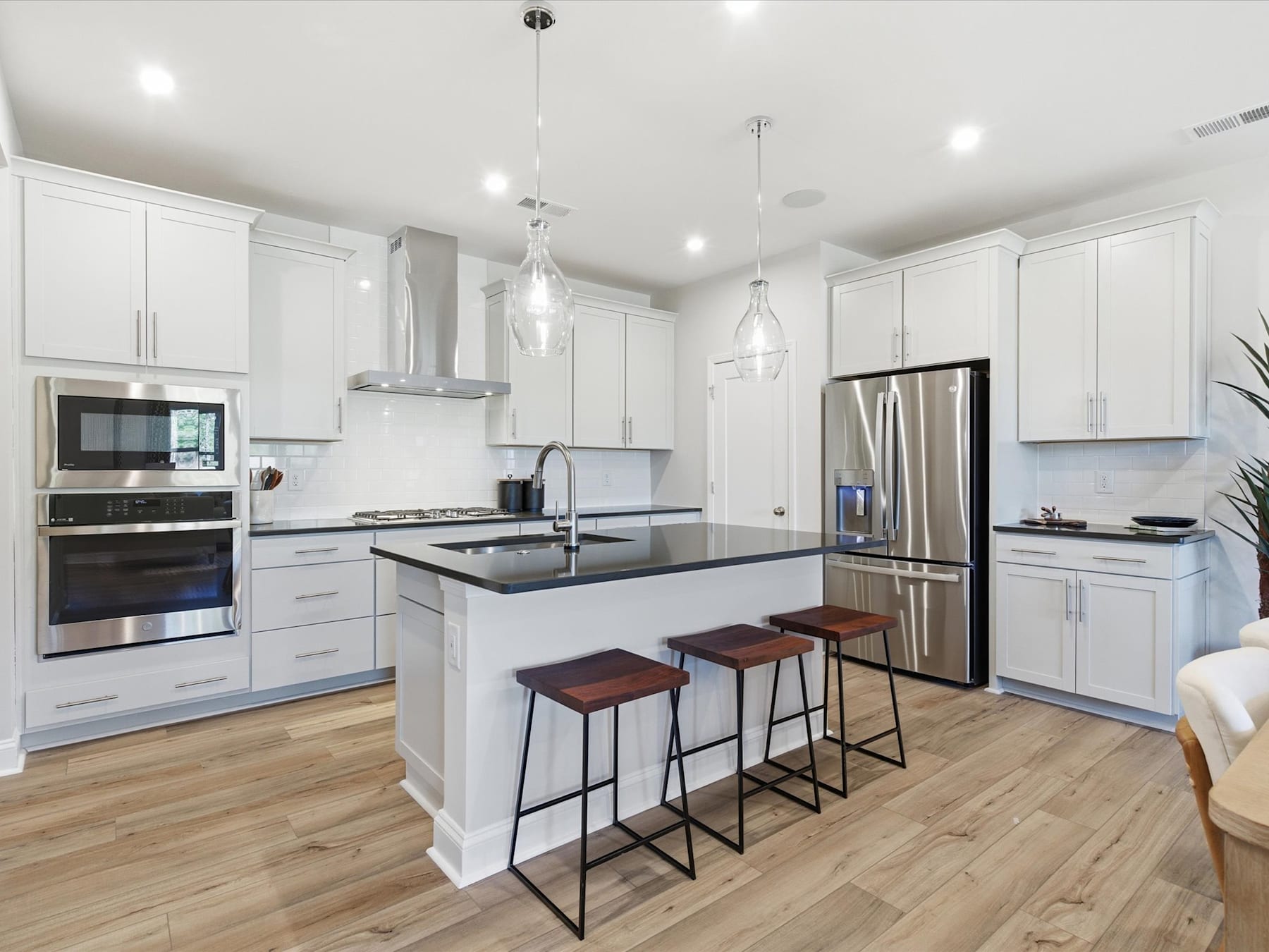 A modern, well-equipped kitchen with white cabinets, stainless steel appliances, and a central island with bar stools, set against a hardwood floor.