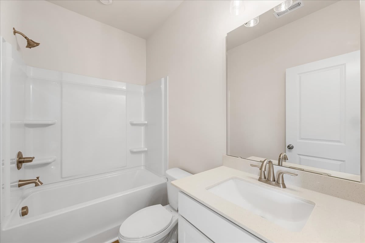 A clean, modern bathroom with a white vanity, sink, and toilet, along with a bathtub and shower enclosure.