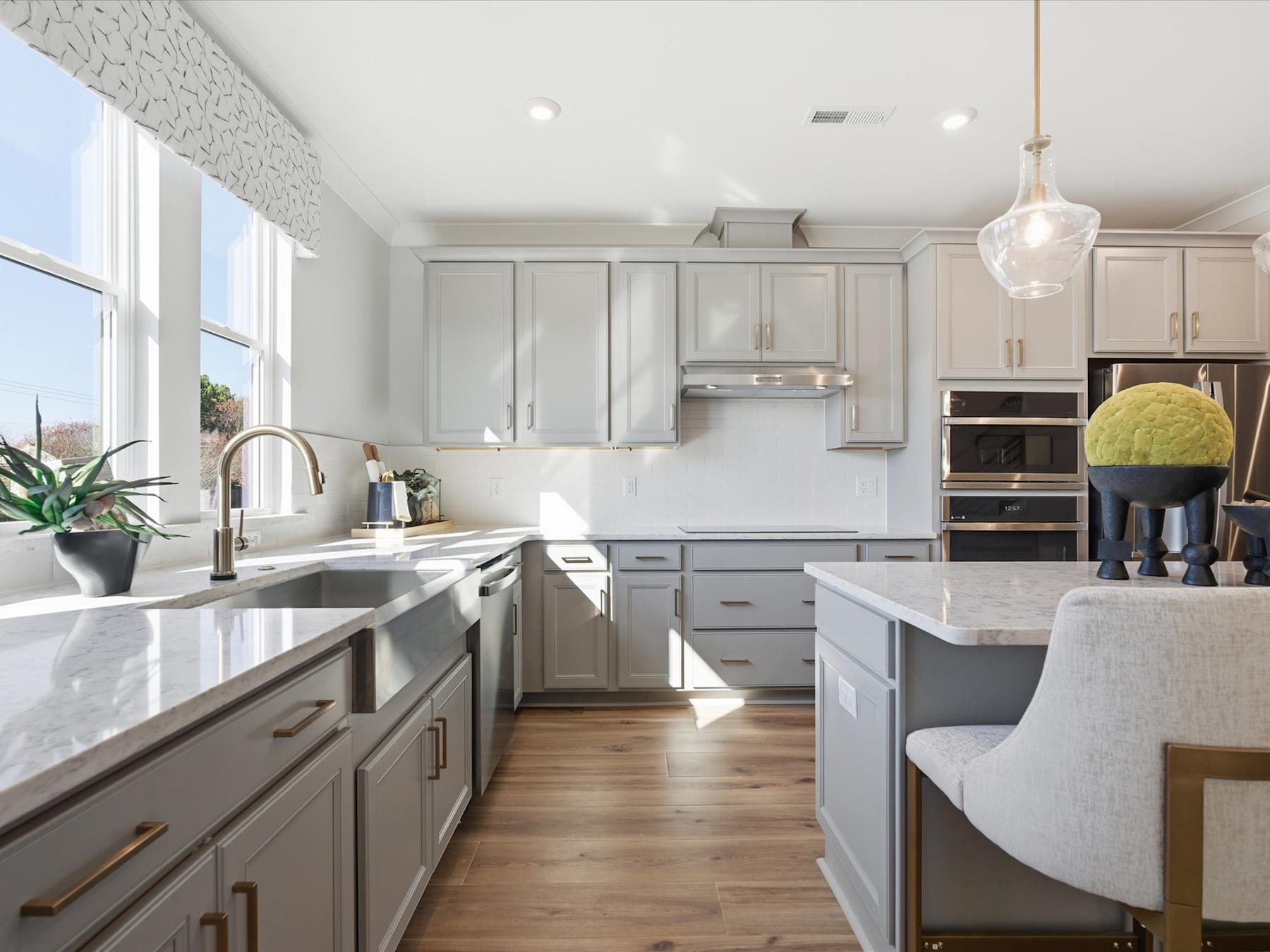 A modern, well-lit kitchen with gray cabinets, stainless steel appliances, and a large window providing natural light.