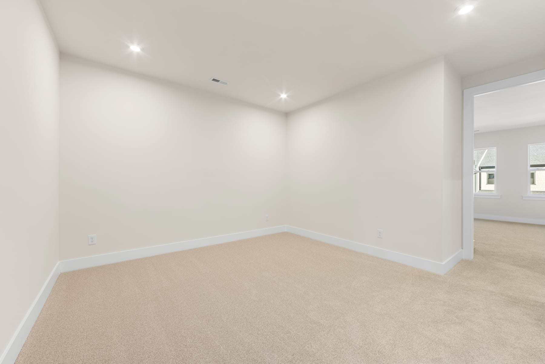 A spacious, well-lit room with white walls and a beige carpeted floor, creating a clean and minimalist atmosphere.
